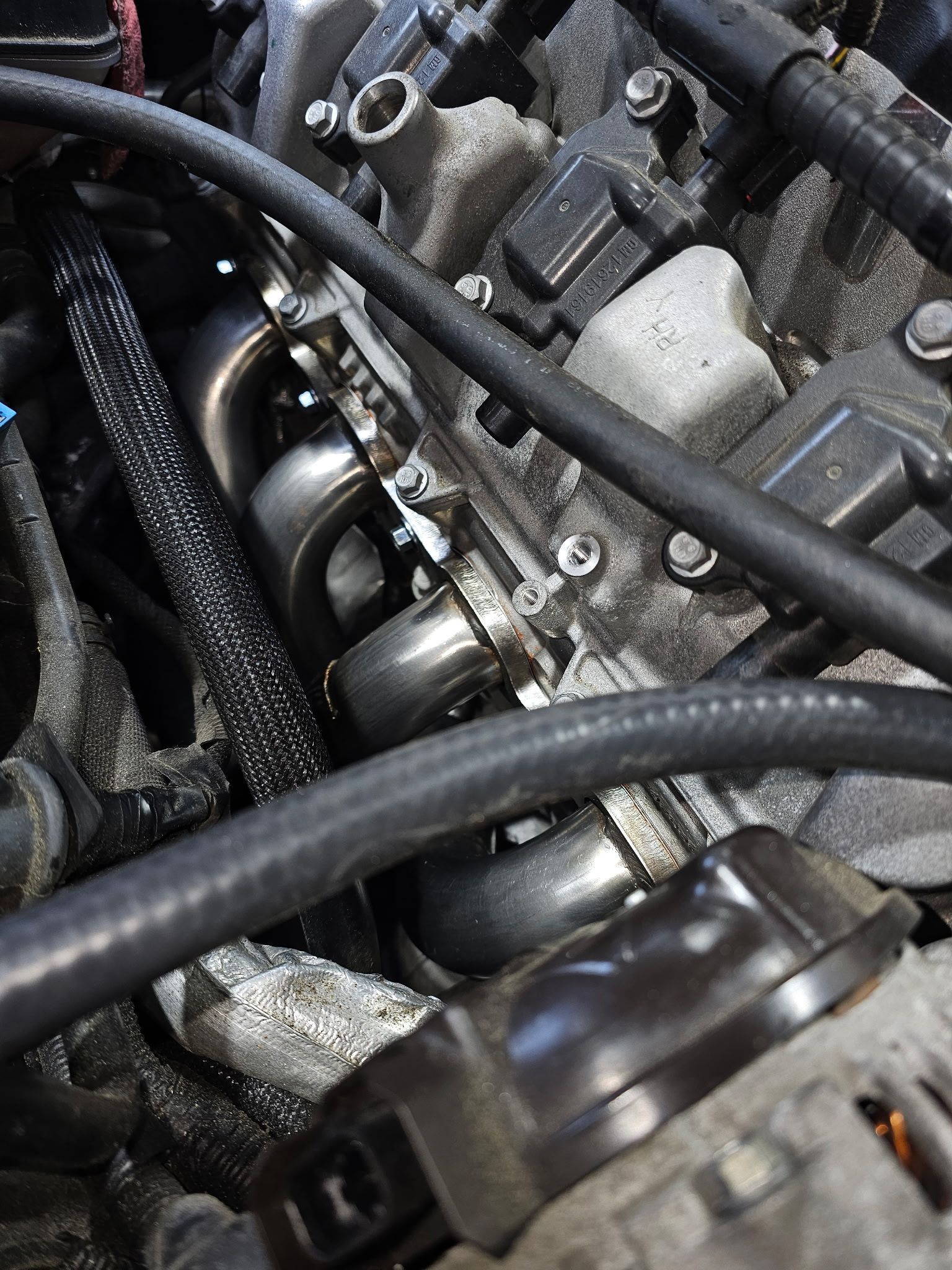 Close-up of a car engine with black hoses, metal parts, and wiring.