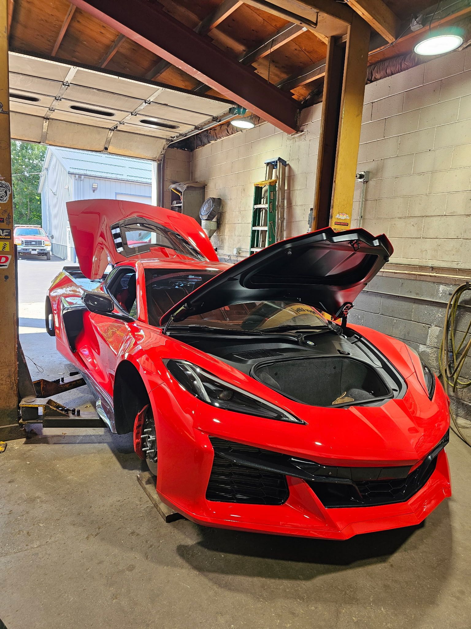 Red sports car with hood open in a garage, showing a black front hood and red body.