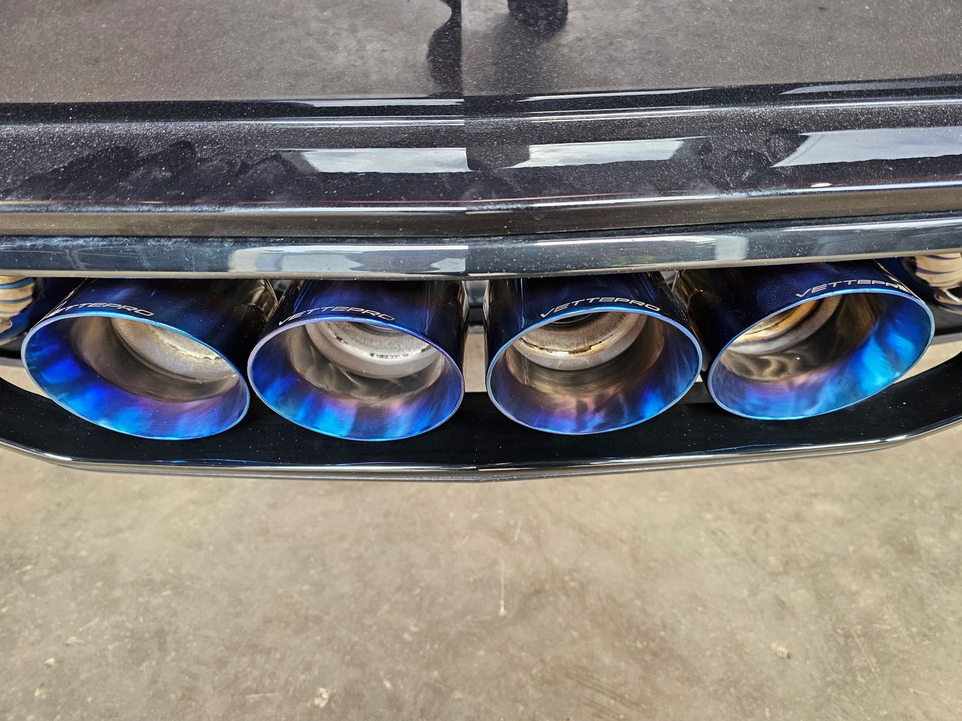 Close-up of a car’s four blue-tinted exhaust tips beneath the rear bumper.