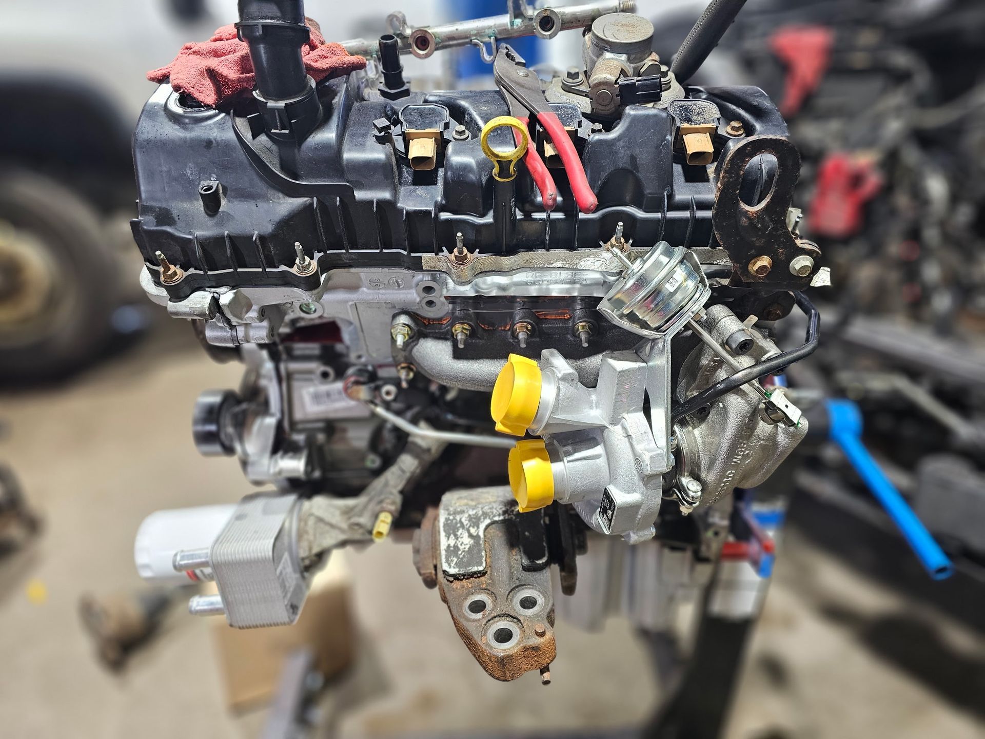 Close-up of a disassembled car engine on a workshop floor, with hoses and metal parts visible