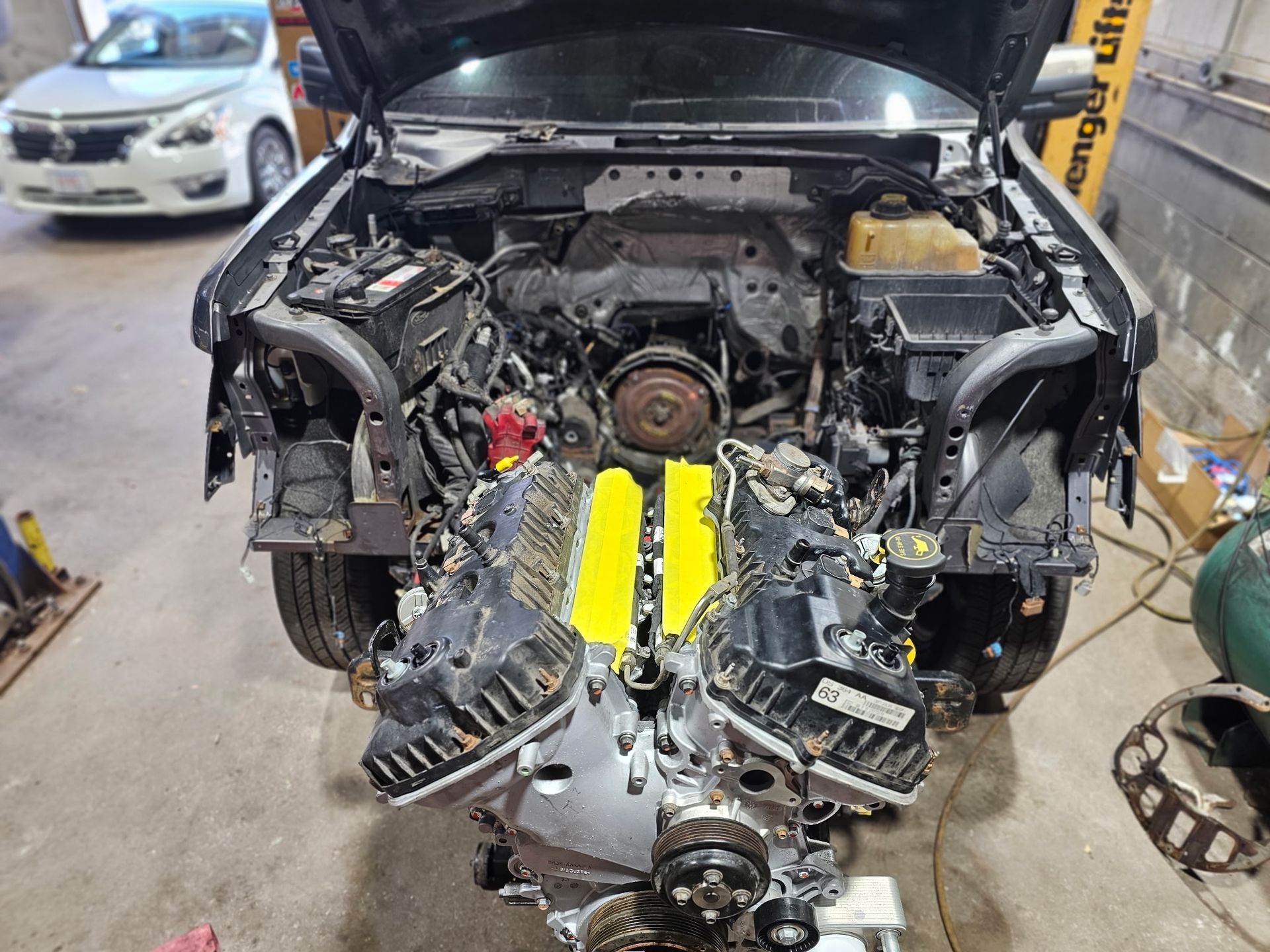 Severe front-end car damage in an auto shop, with engine exposed and parts removed.