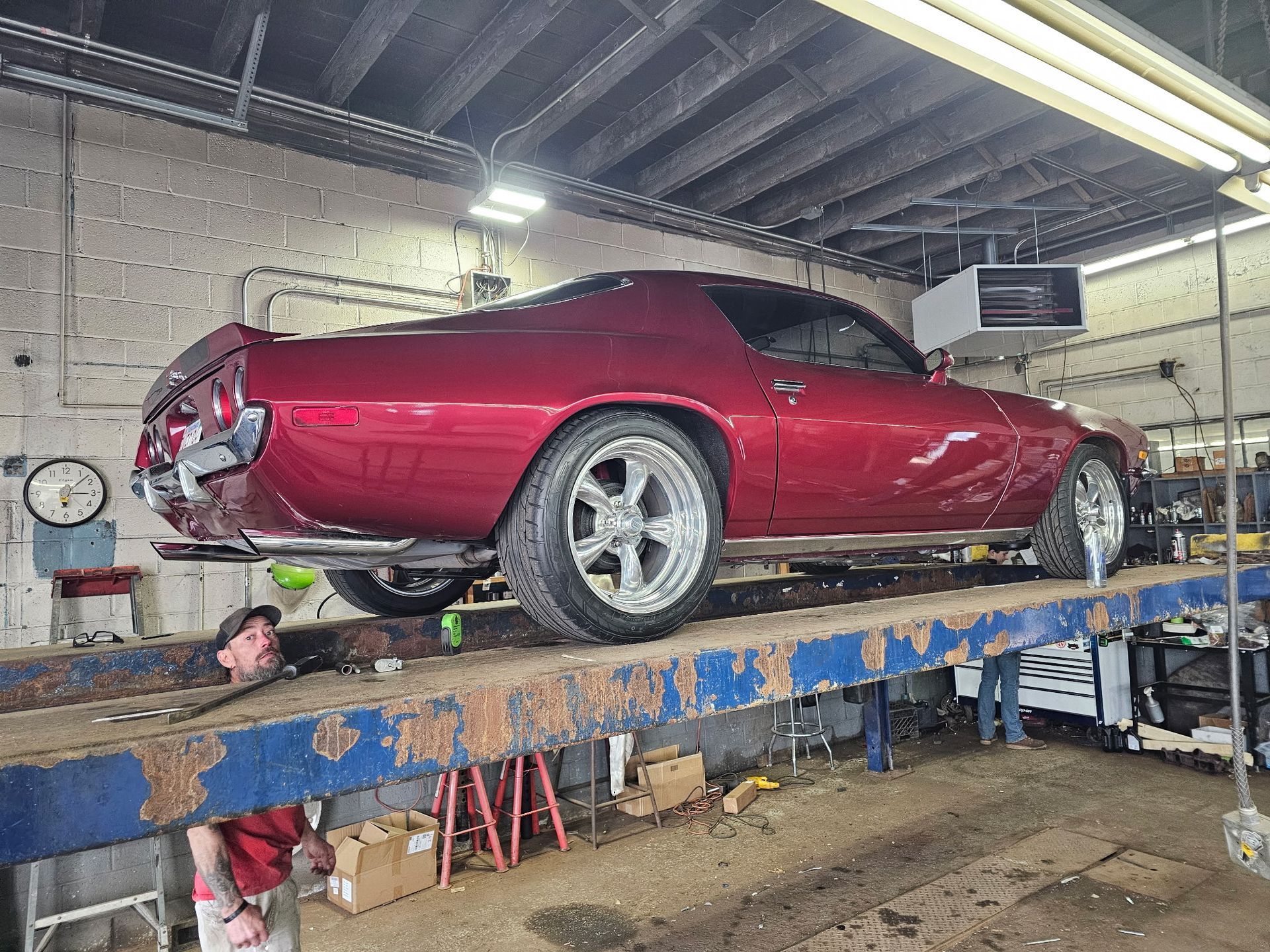 Red sports car on a blue auto lift inside a garage, with a mechanic partially visible below.