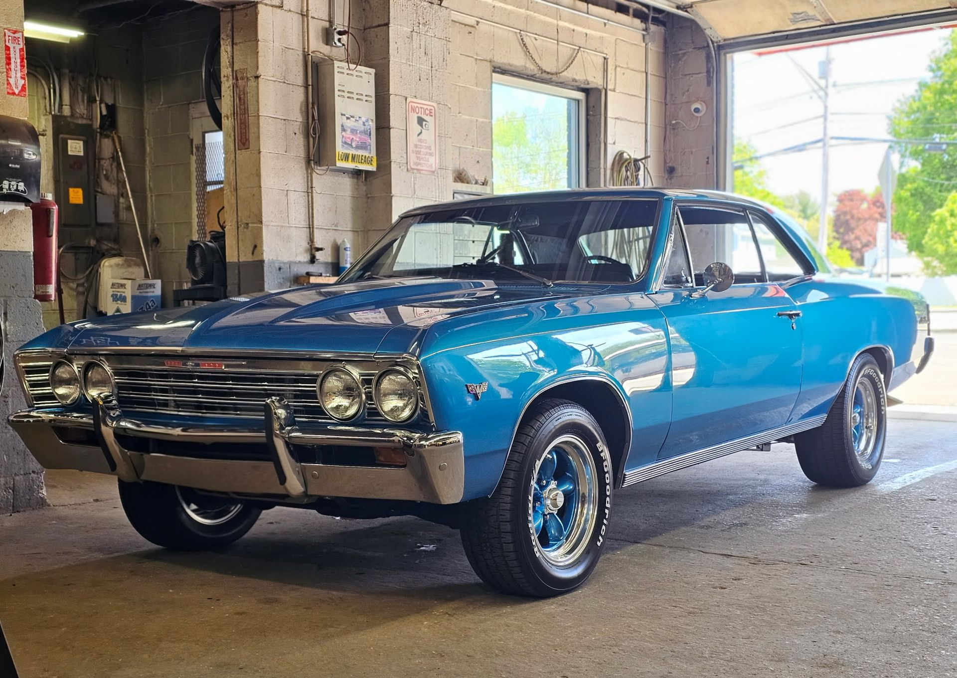 Blue classic muscle car parked inside a garage, front-left view, with chrome trim and raised rear tires