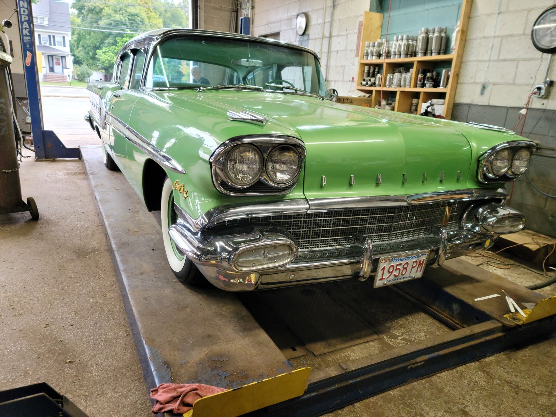 Mint-green classic car in a garage, front view with chrome details and raised on a lift.