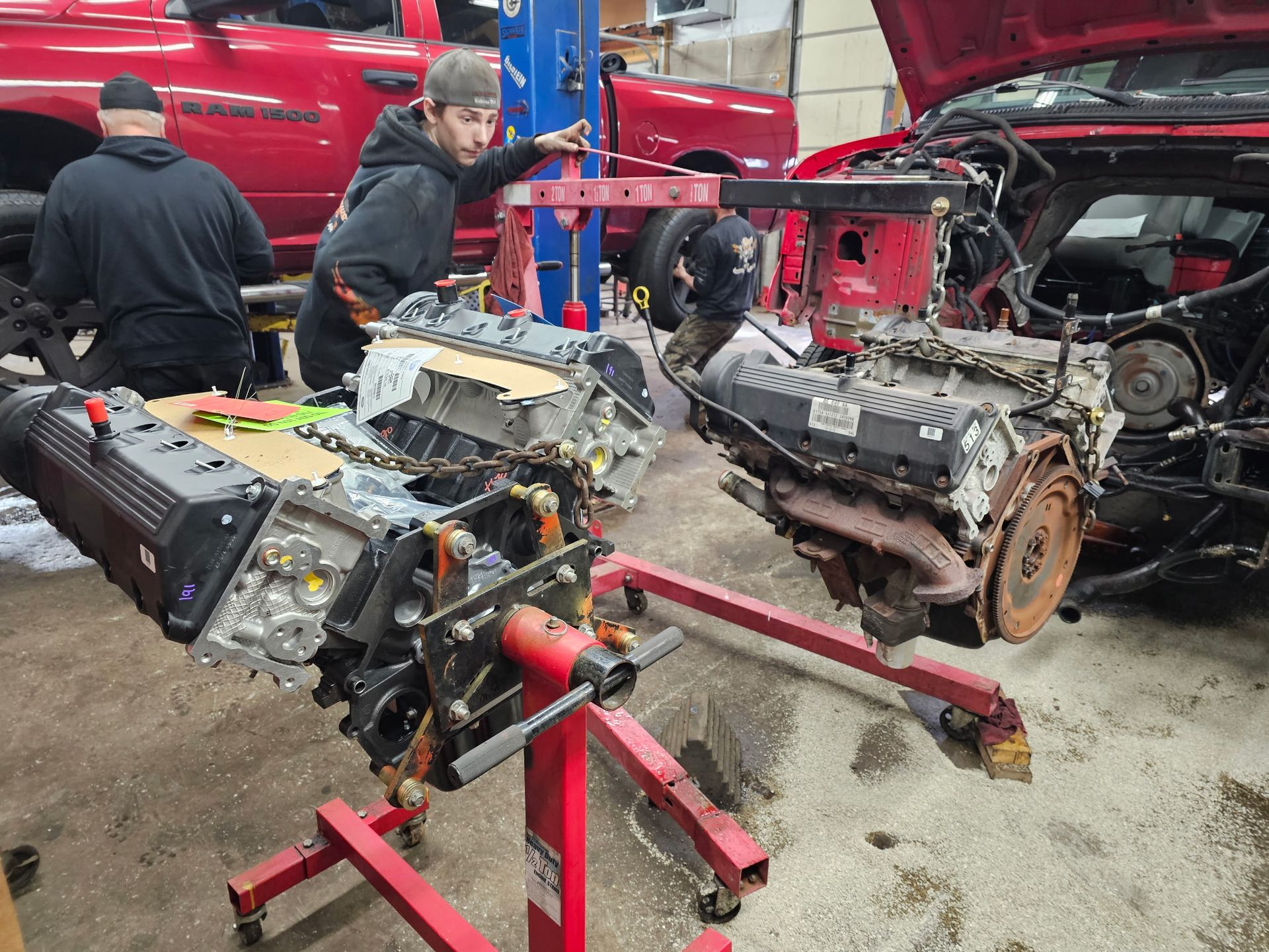 Auto shop with mechanics working on several removed car engines and transmissions on stands.