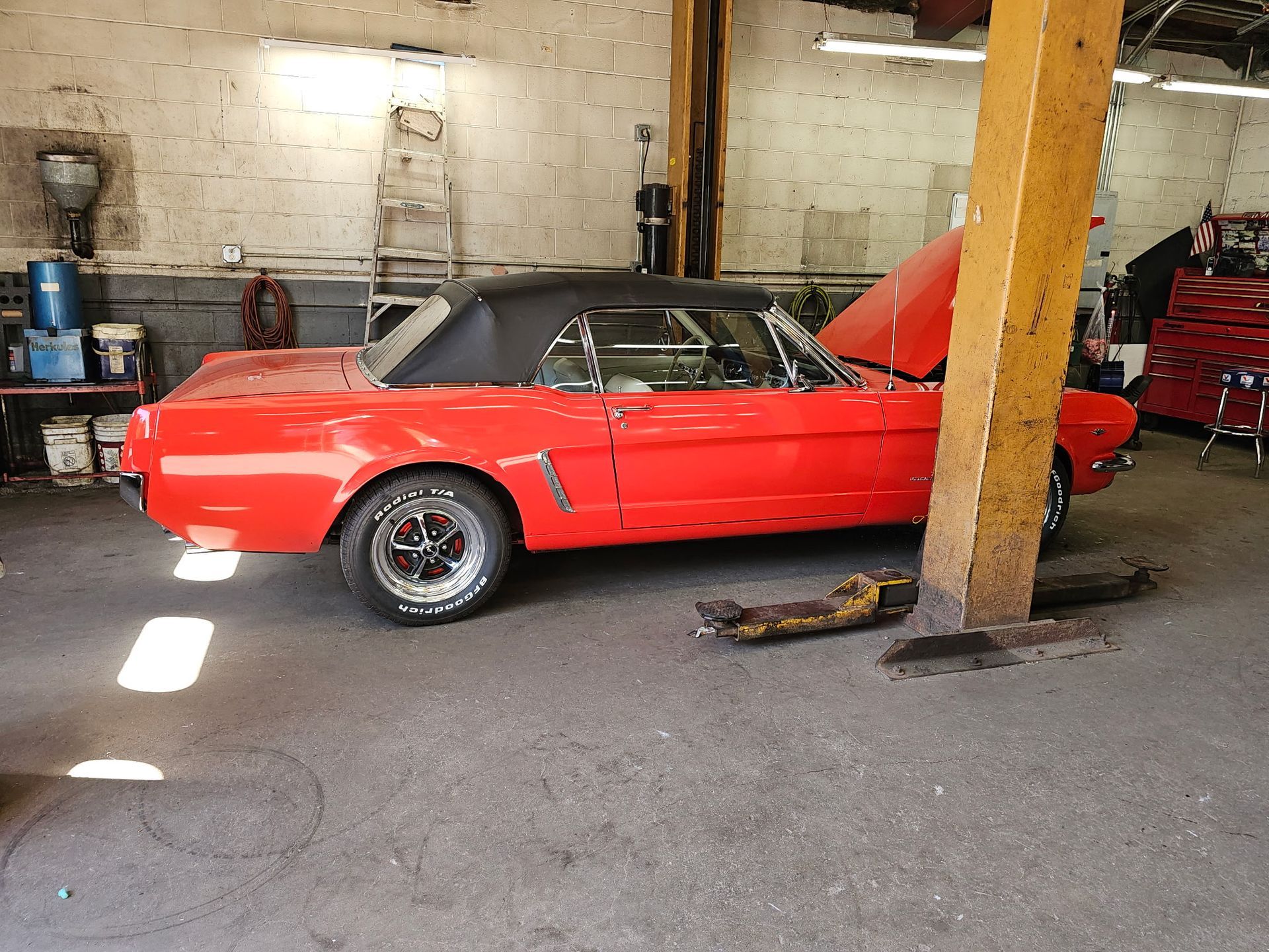 Red classic convertible parked in a garage beside a wooden support post.