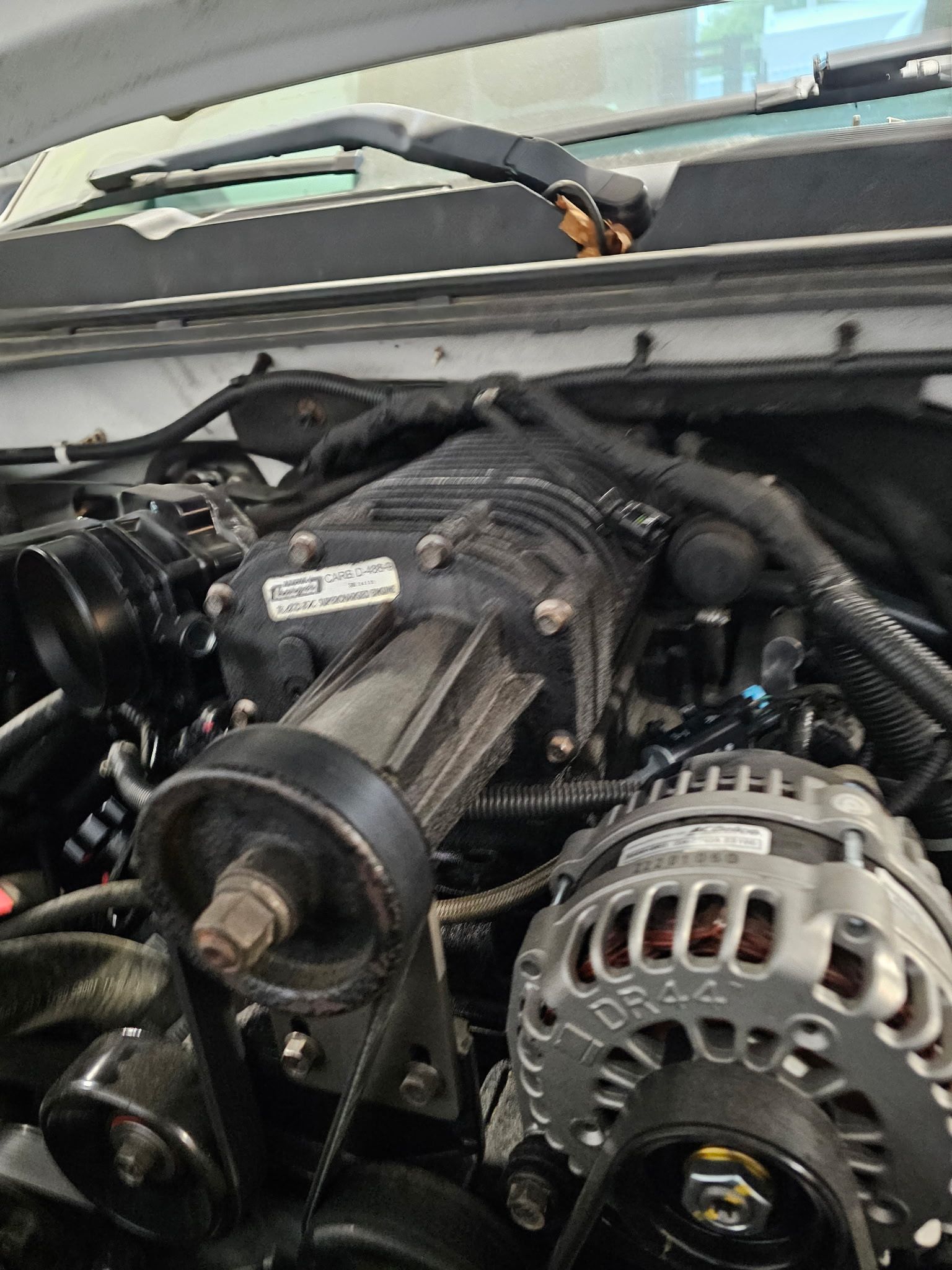 Car engine bay with exposed alternator, belts, and hoses under the hood