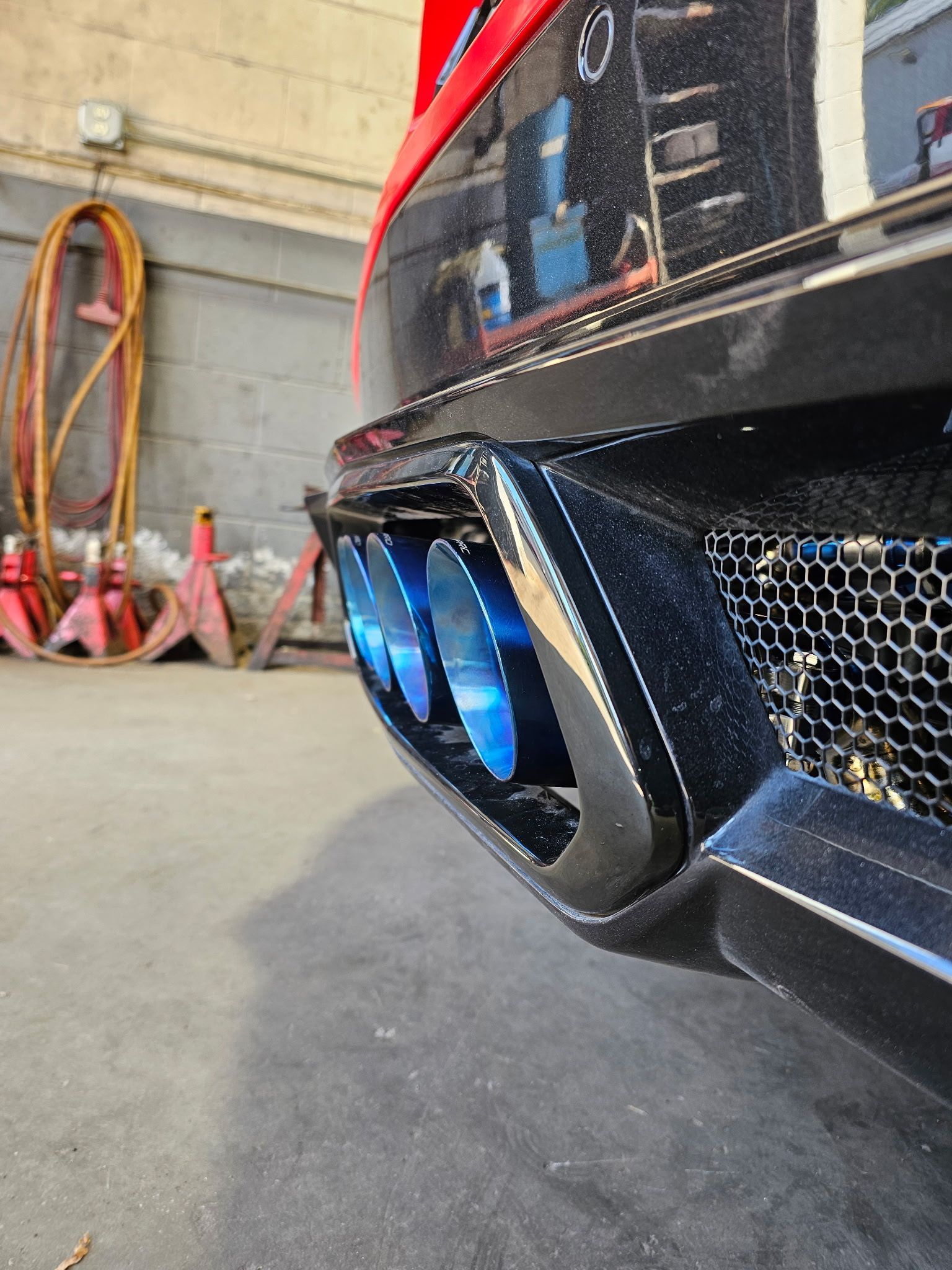 Close-up of a black sports car rear bumper with blue exhaust tips in a garage