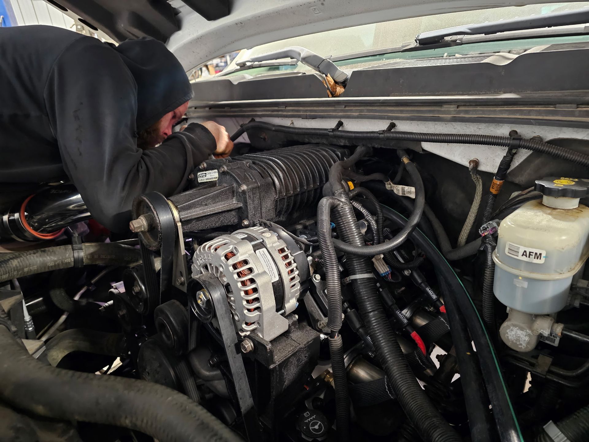 Mechanic working under a vehicle hood, inspecting engine components and wiring