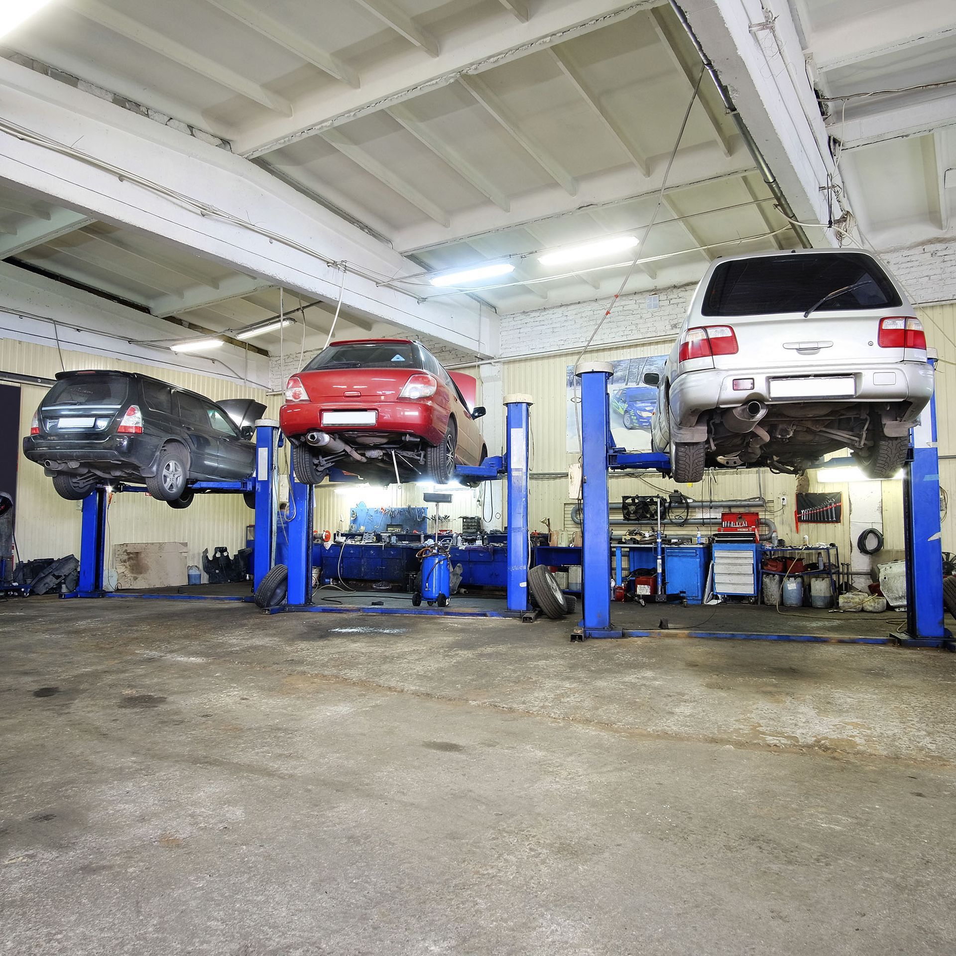 Auto repair shop with three cars lifted on blue hoists inside a large garage