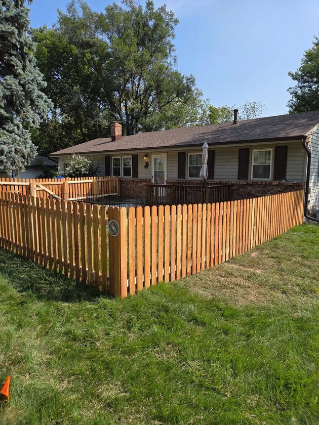 Small house with a wooden privacy fence and grassy yard under a sunny blue sky