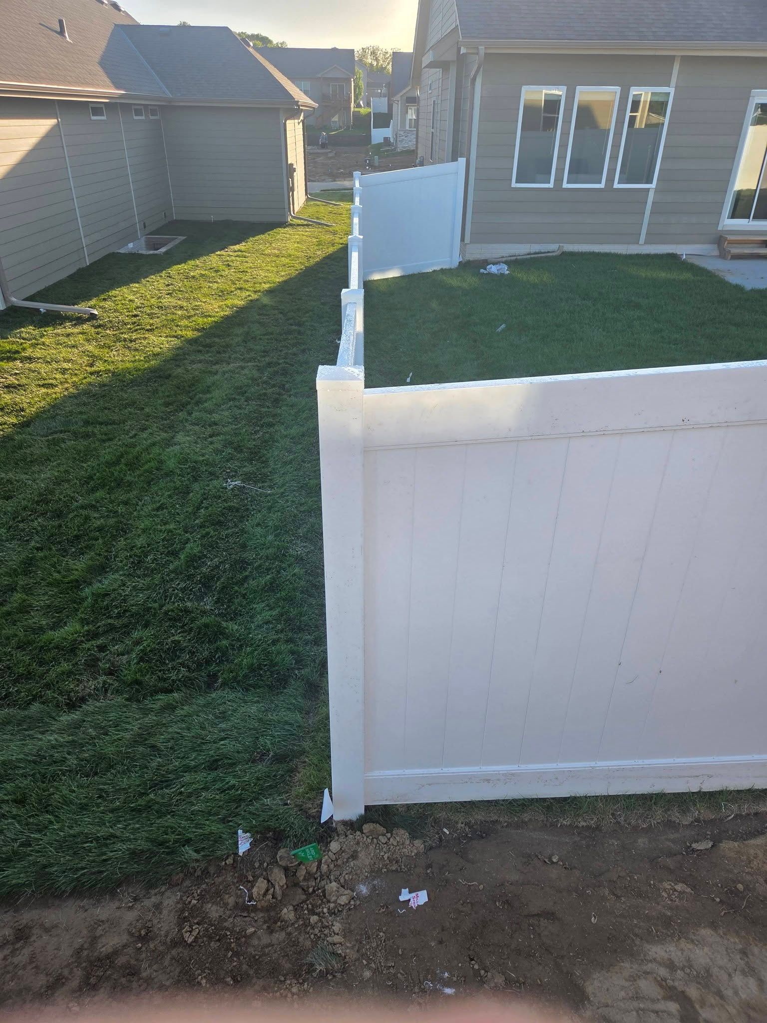 Backyard with white fence, green grass, and a gray house in sunlight