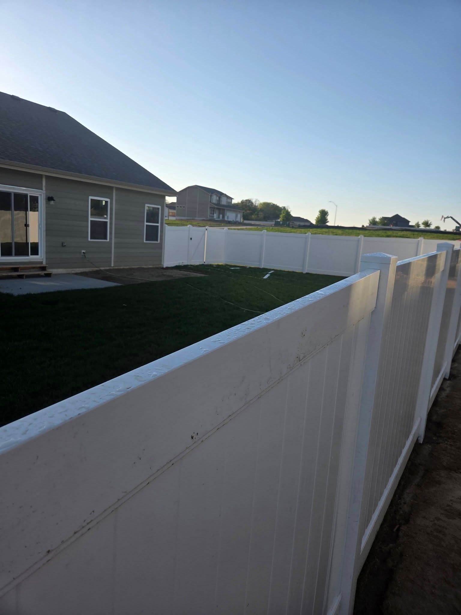 White vinyl fence along a house and yard under a clear sky at sunset
