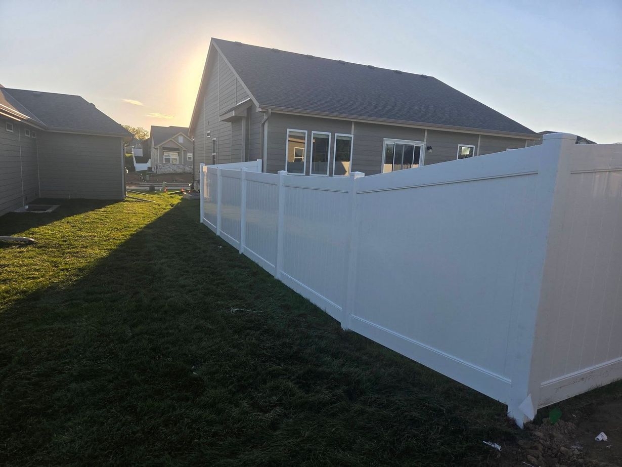 White vinyl fence beside a gray house in a sunlit suburban yard