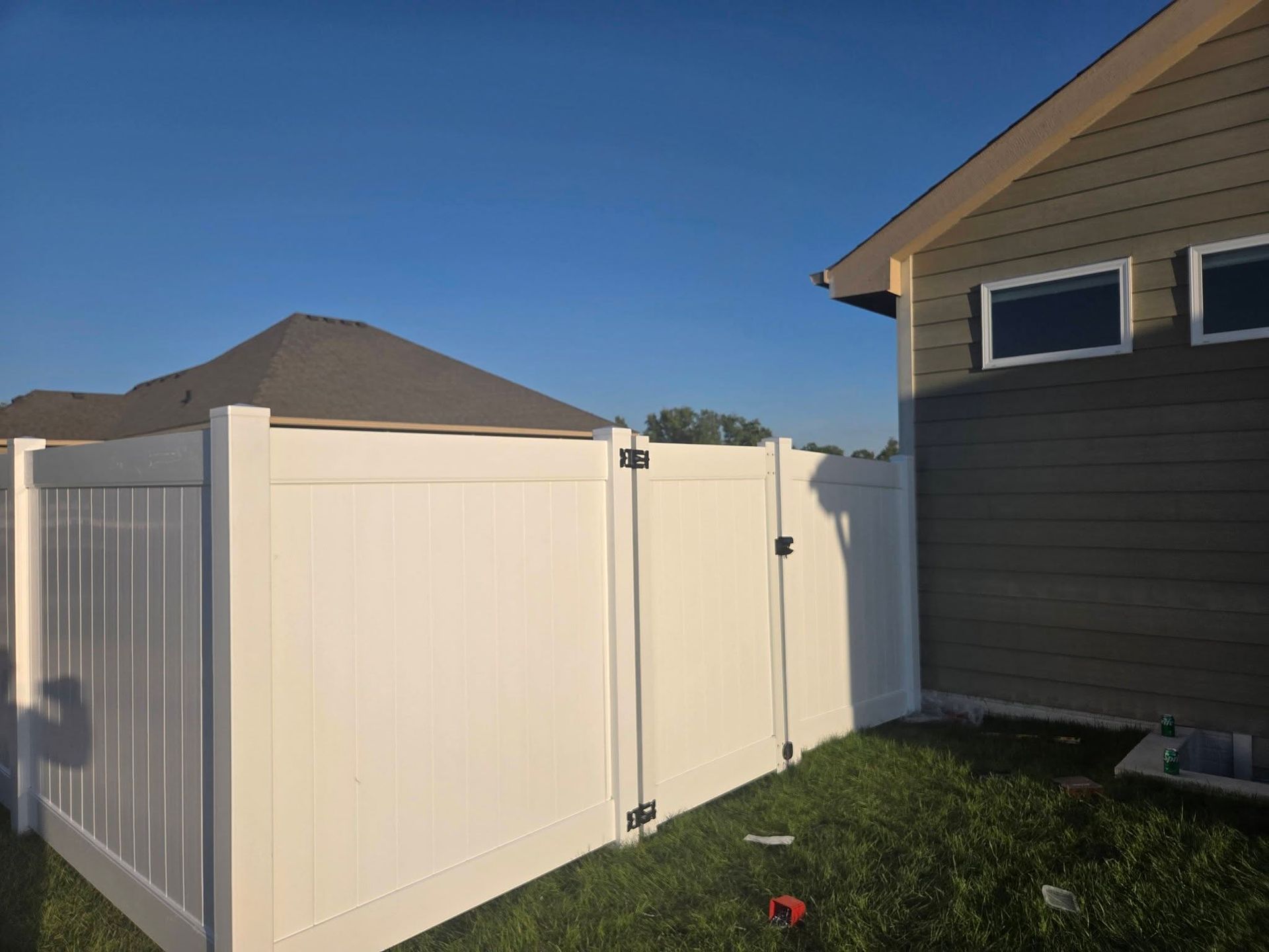 White vinyl fence around a backyard beside a house under a clear blue sky