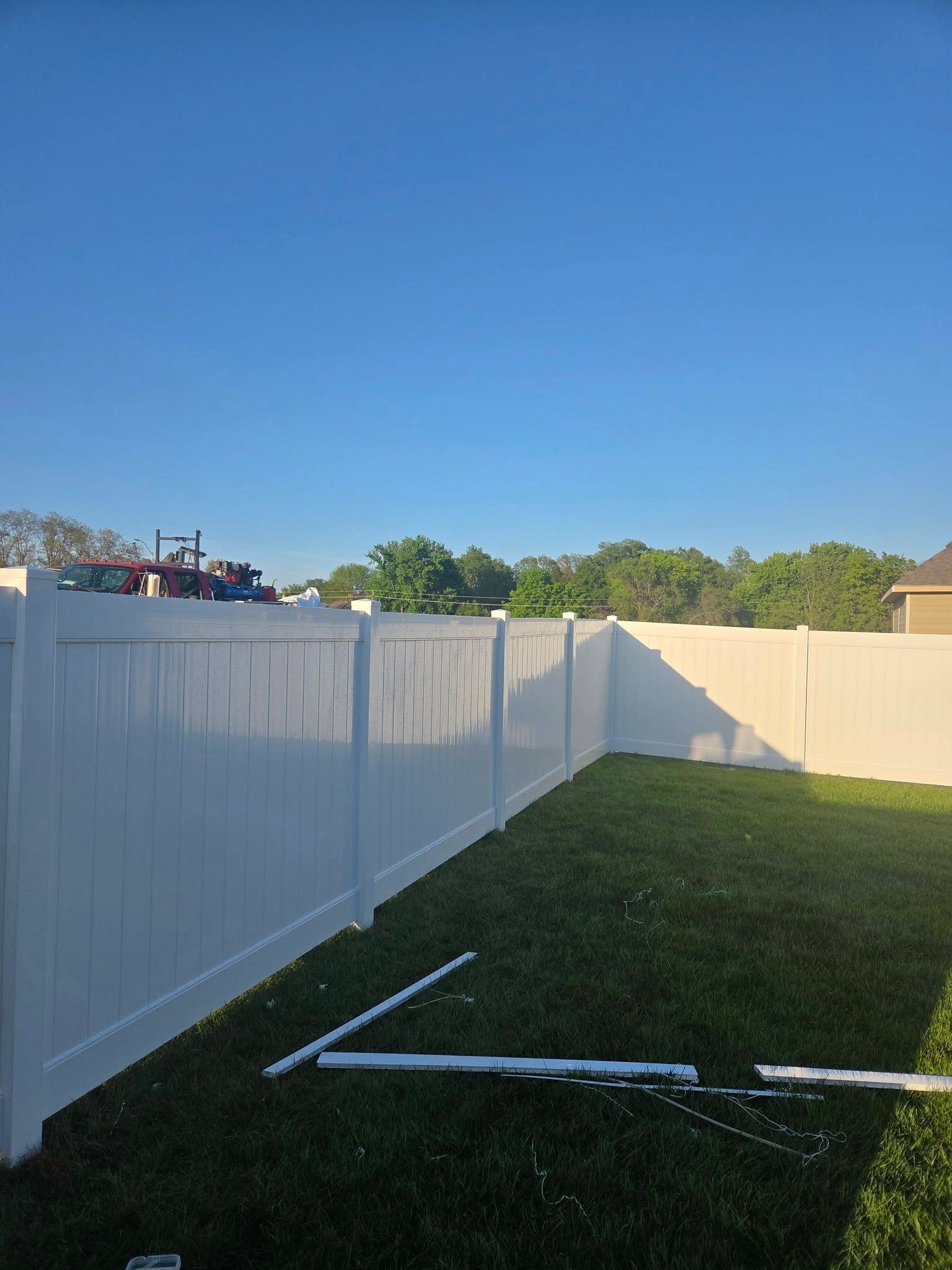 White vinyl fence along a grassy backyard under a clear blue sky with a small white pipe on the ground