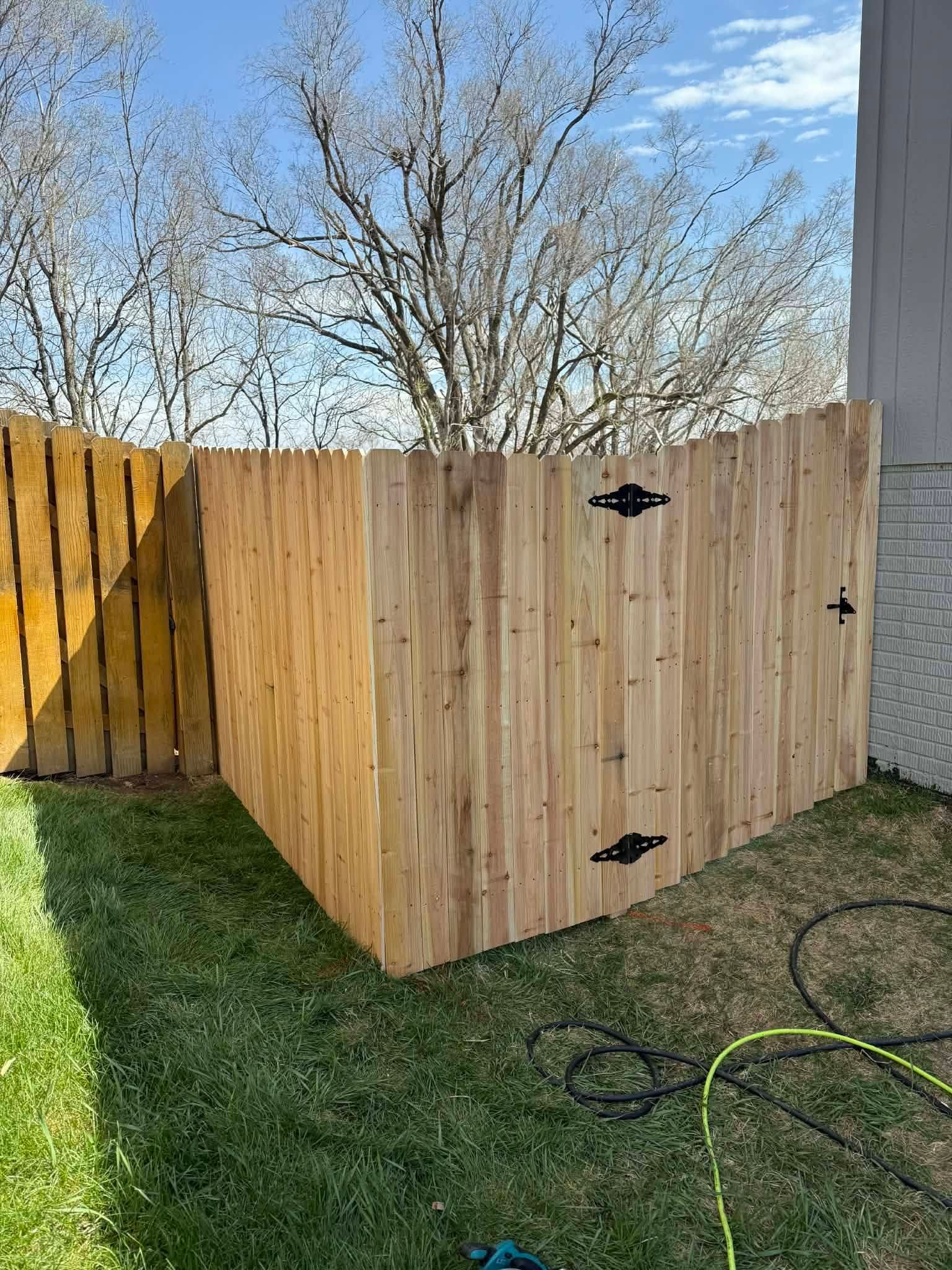 Wooden outdoor enclosure with black hinges on a sunny backyard patio, trees in the background.