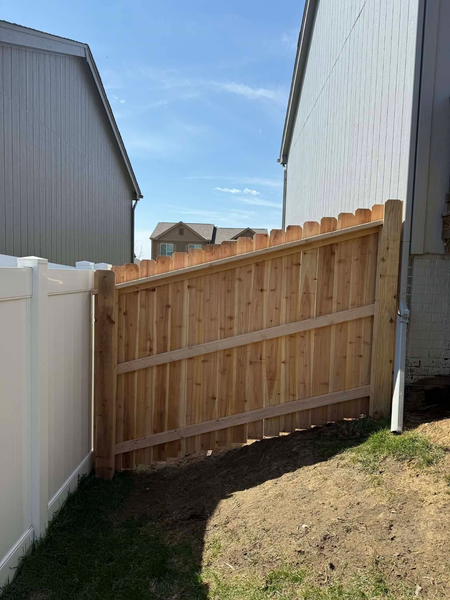 Wooden privacy fence between two homes, with grass and a small yard under a blue sky.
