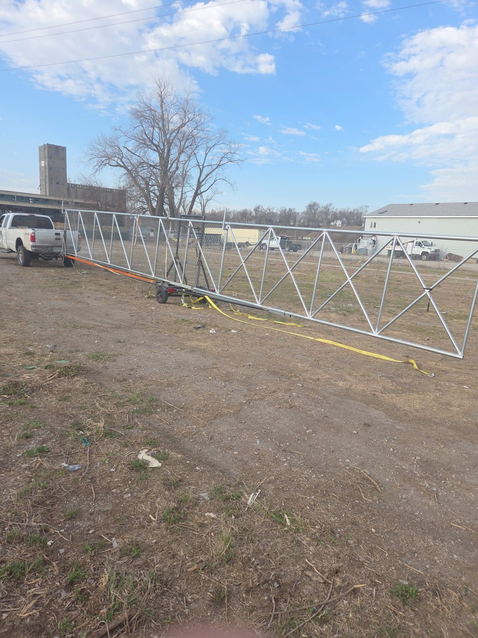 White lattice fence panels lined up on a gravel lot beside a road under a blue sky.