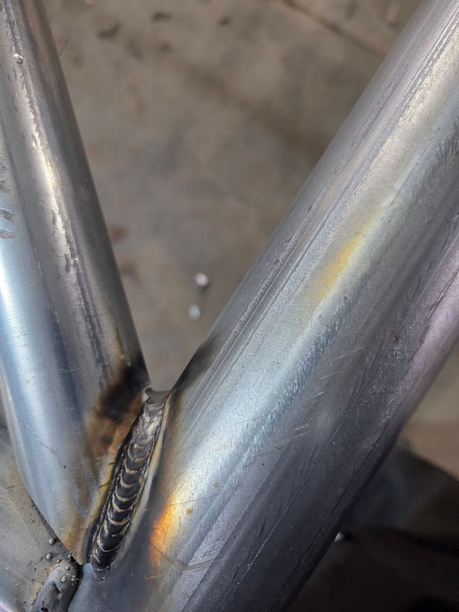 Close-up of a welded metal joint with two silver tubes forming a V-shape