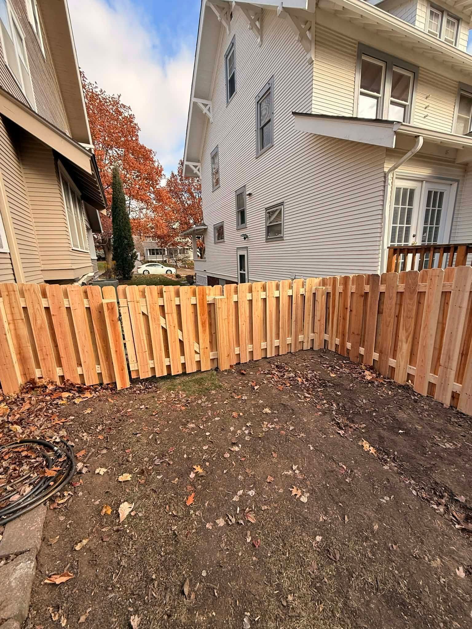 Backyard garden bed with fresh soil, wooden fence, and houses beside a gray tarp-covered structure