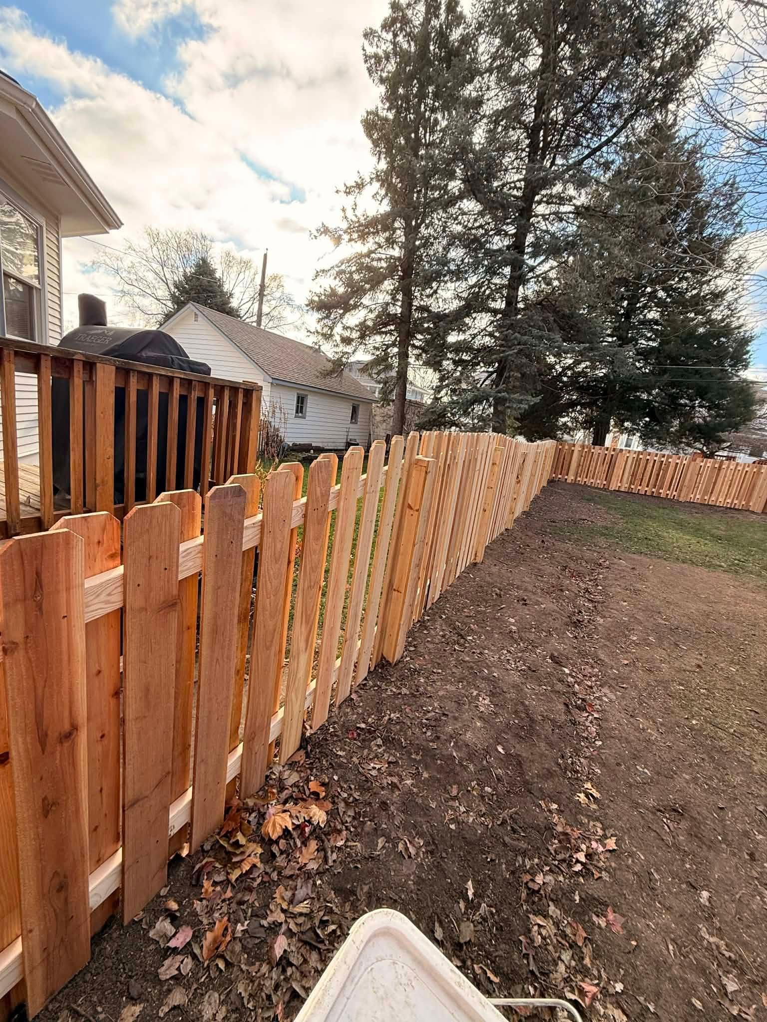 Wooden fence along a dirt yard beside a house, with trees in the background.