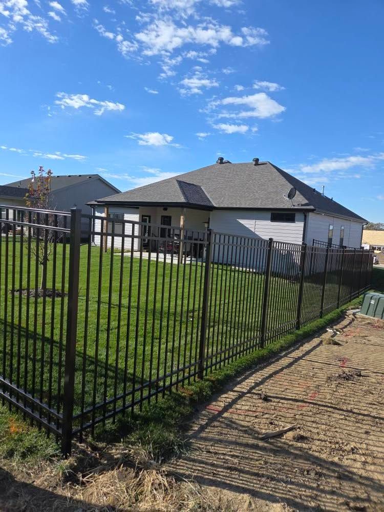 Suburban house with black metal fence, green lawn, and partly cloudy blue sky