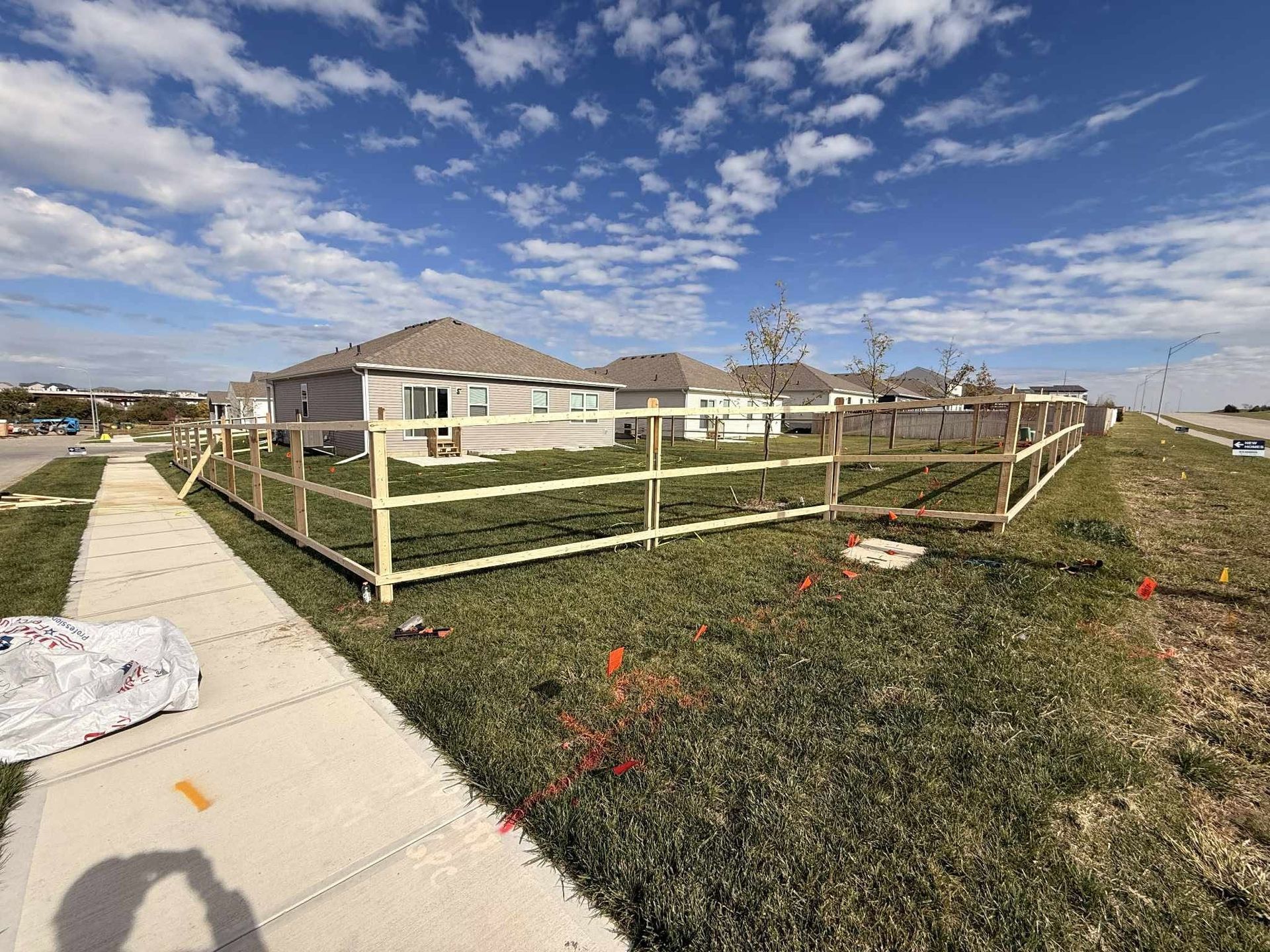 Suburban house with fenced yard beside a sidewalk under a partly cloudy blue sky