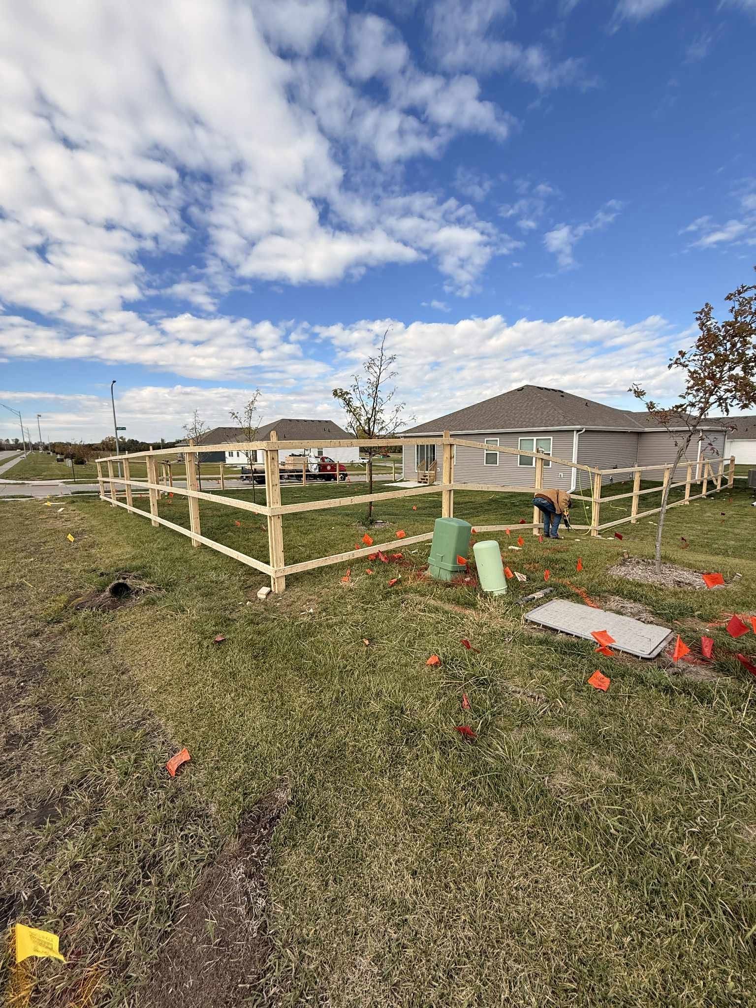 Wooden fence under construction in a grassy yard with scattered tools and a partly cloudy sky.