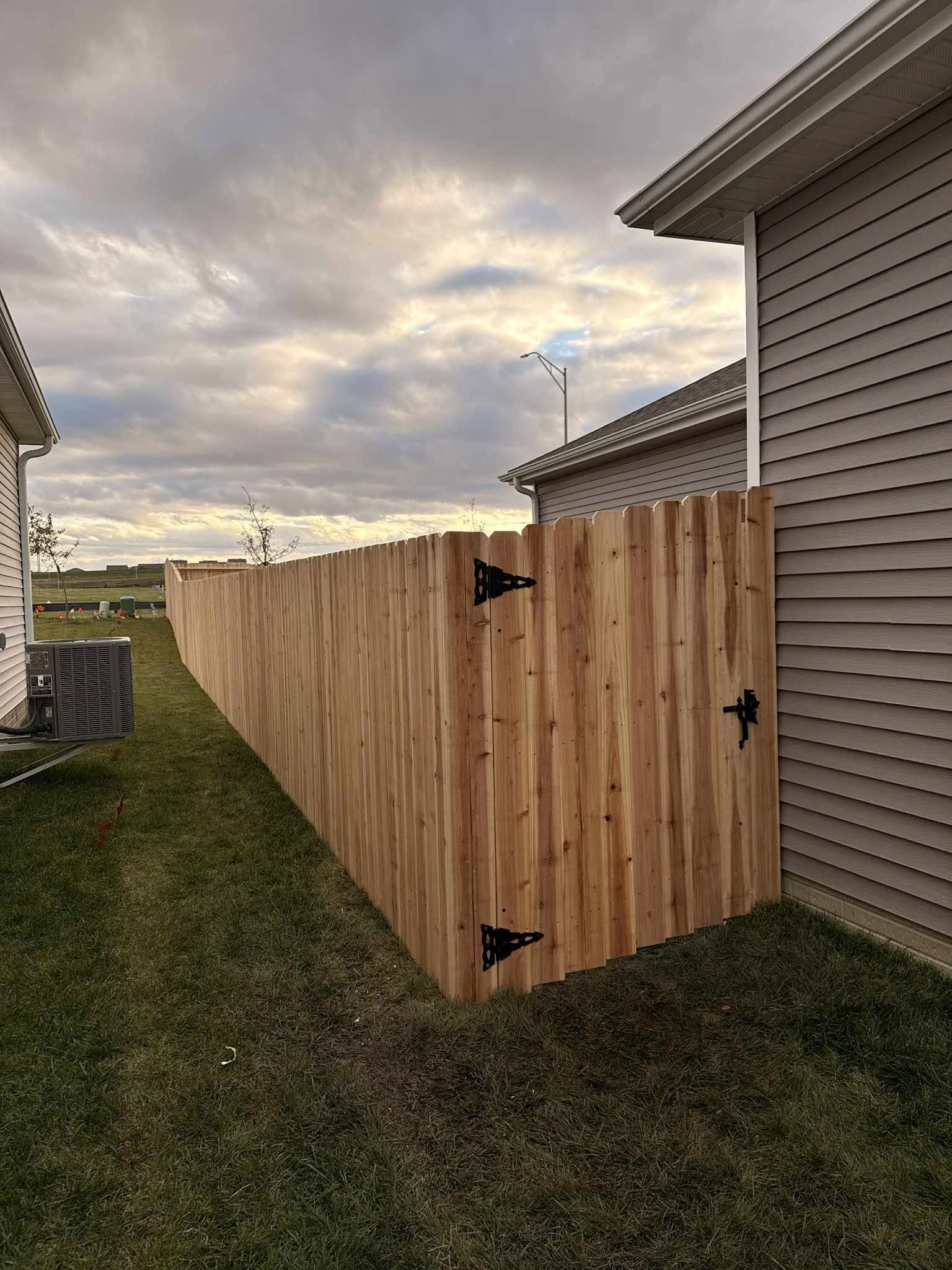 Wooden privacy fence with gate between houses beside a grassy yard under a cloudy sky