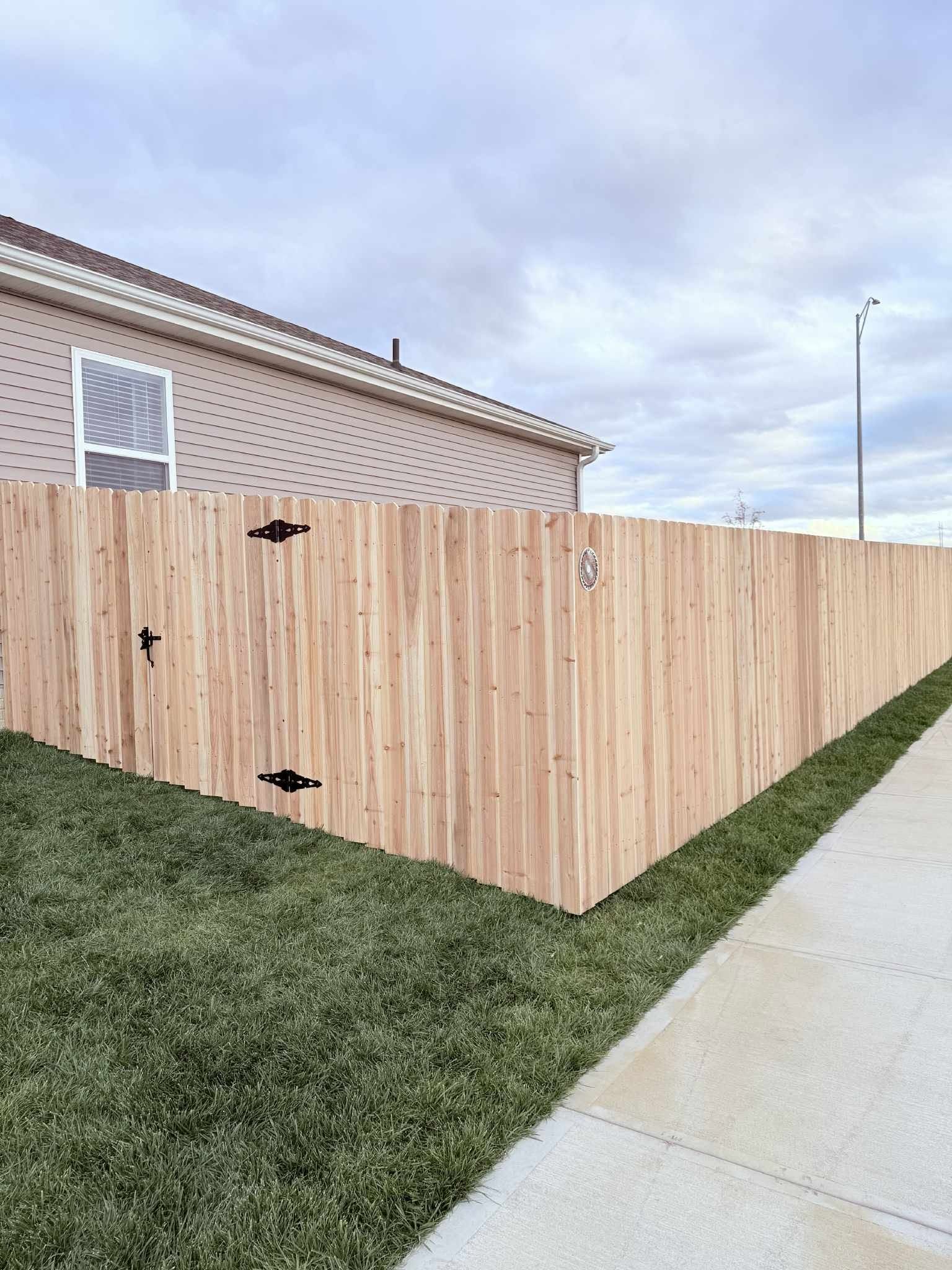Wooden privacy fence along a sidewalk beside a house under a cloudy sky