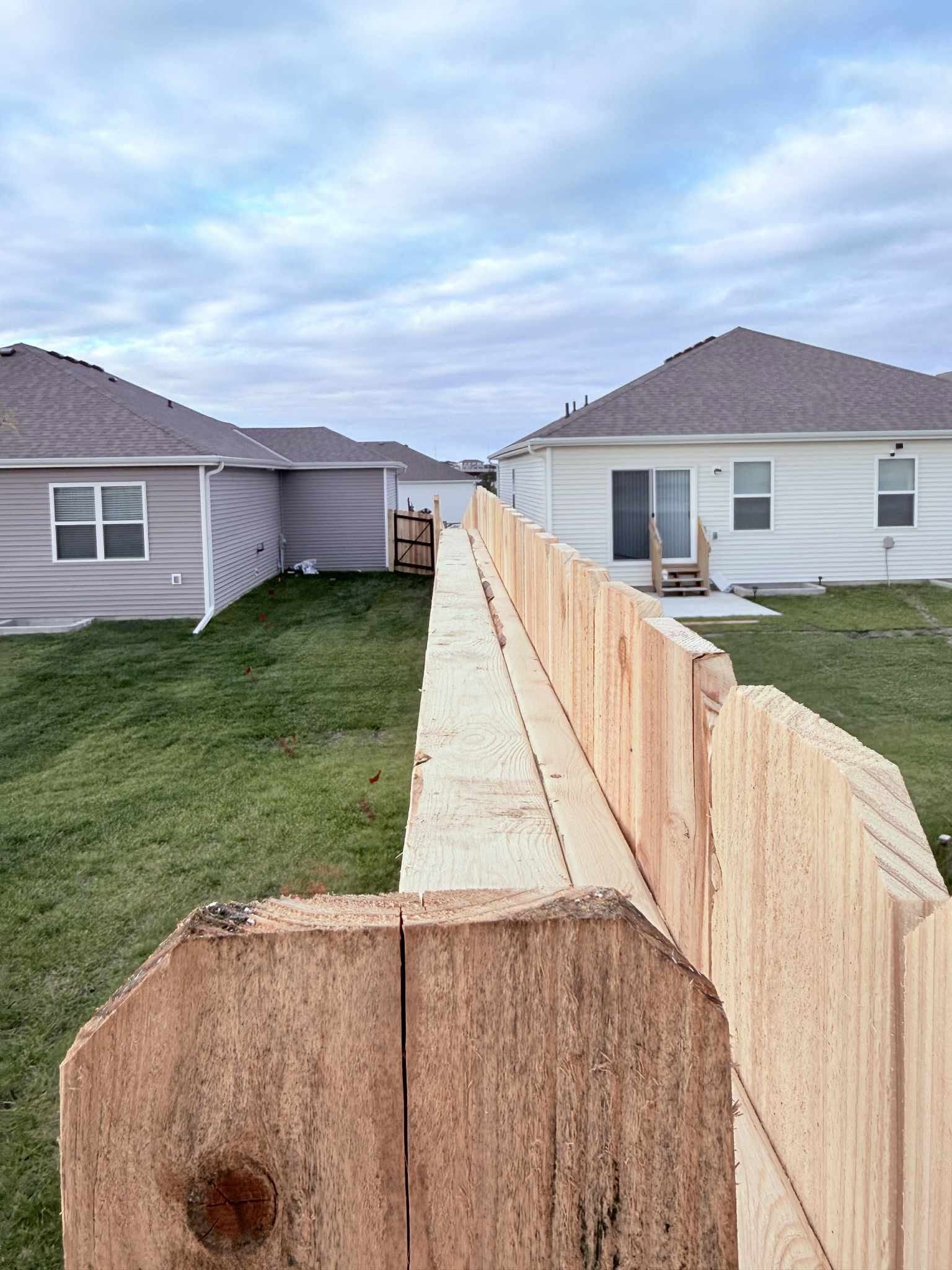 Wooden fence dividing two suburban houses with lawns under a cloudy sky