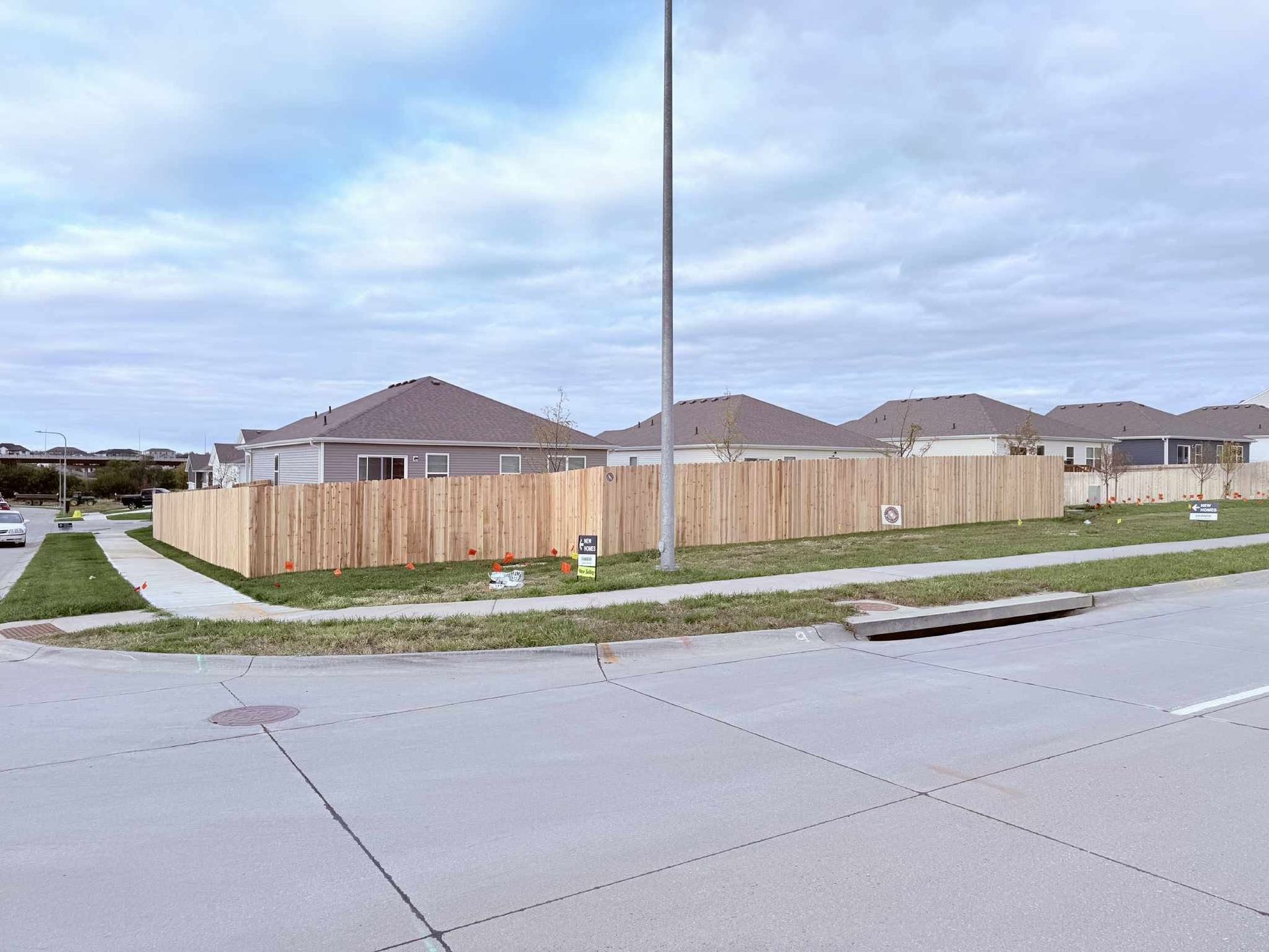 Suburban street with a wooden fence, sidewalk, tall utility pole, and single-story houses under a cloudy sky
