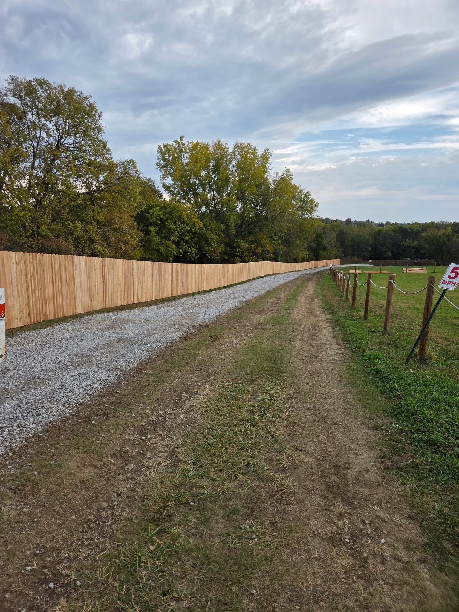 Gravel path beside a wooden fence and grassy field under a cloudy sky