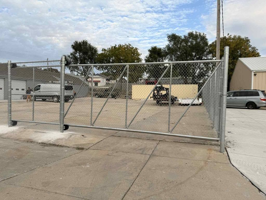 Chain-link gate across a concrete lot with parked vehicles and buildings behind it