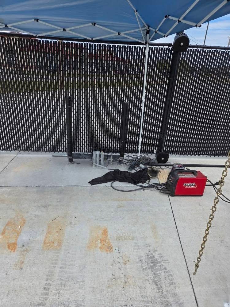 Outdoor concrete deck with chain-link fence, blue canopy, coiled rope, and a red toolbox near a chain barrier