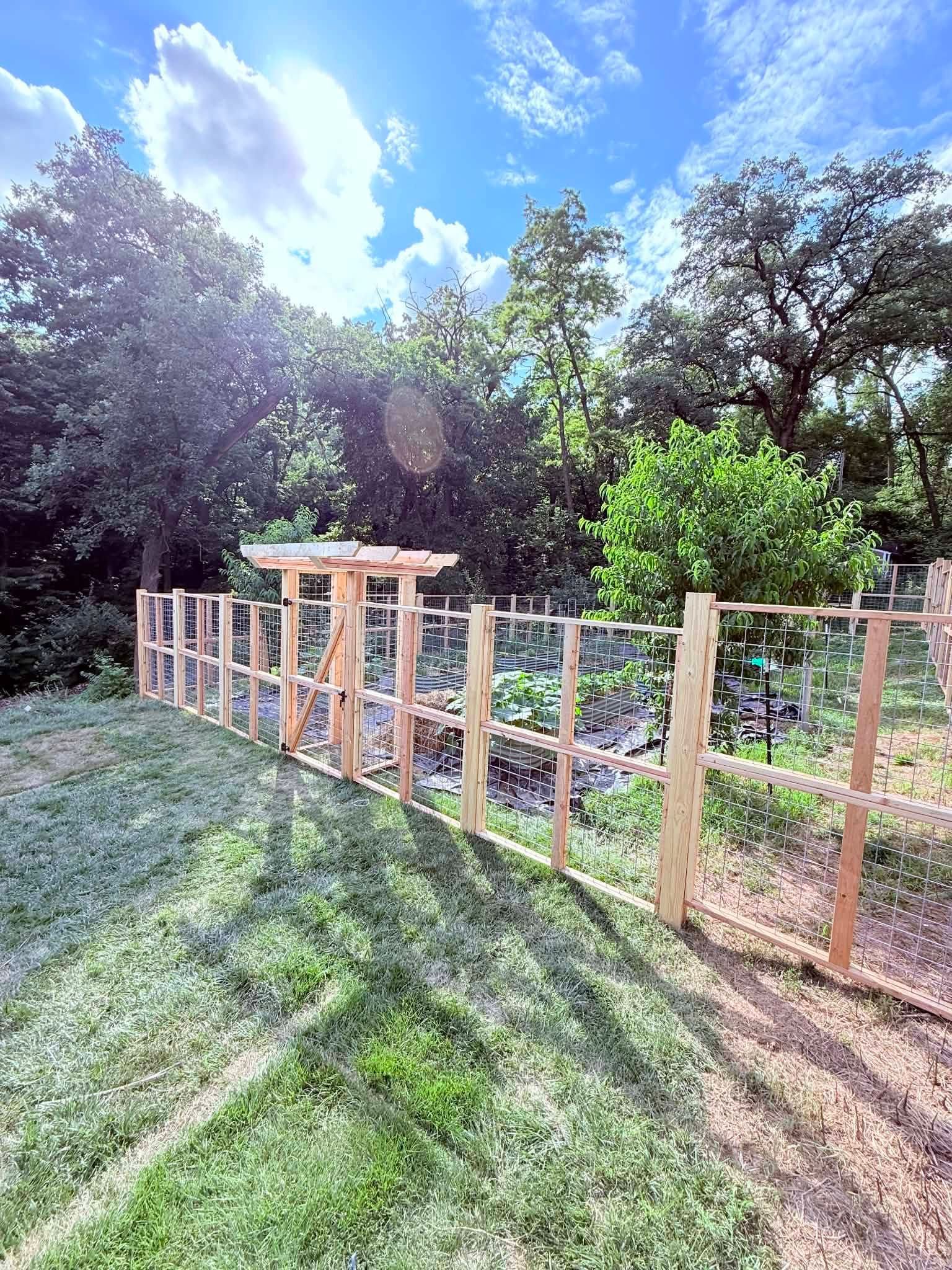 Wooden fence under construction along a grassy path beside trees on a sunny day