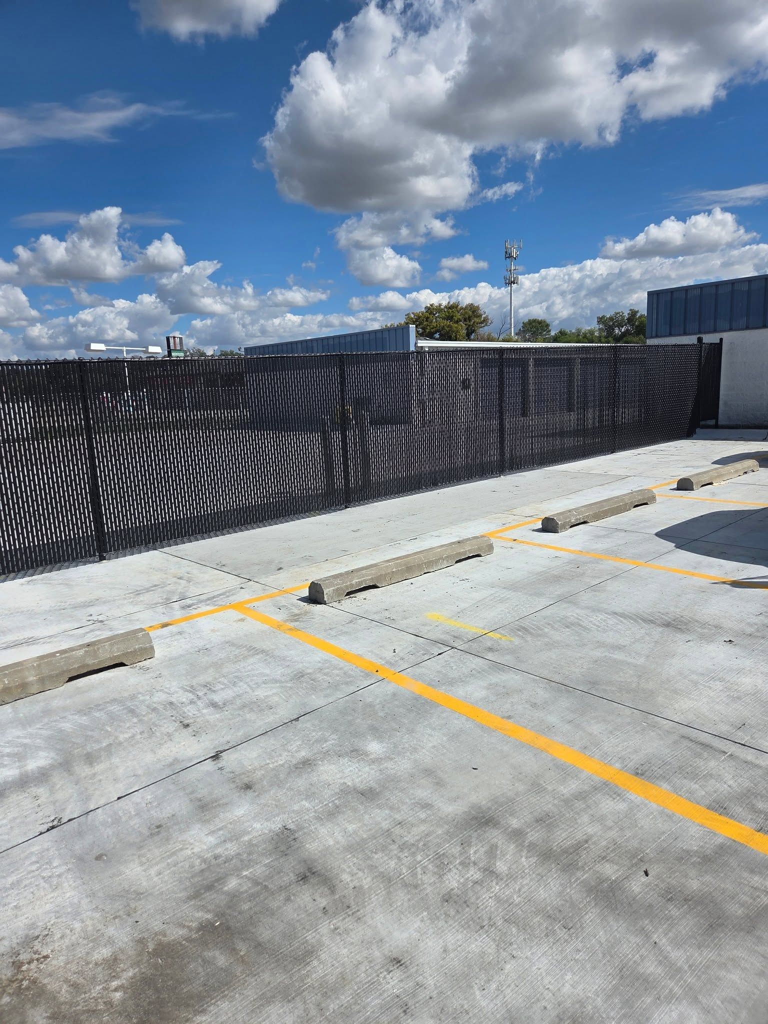 Black metal fence with white wave patterns beside a concrete parking lot under a blue sky with clouds