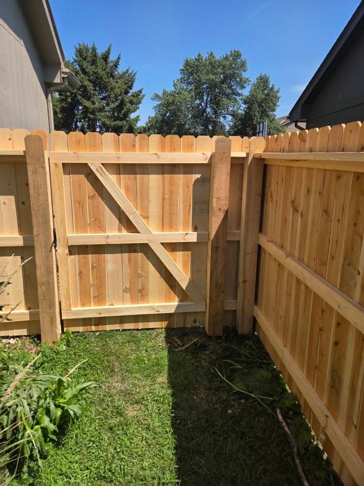Wooden backyard fence gate opening onto a small grassy yard under a blue sky