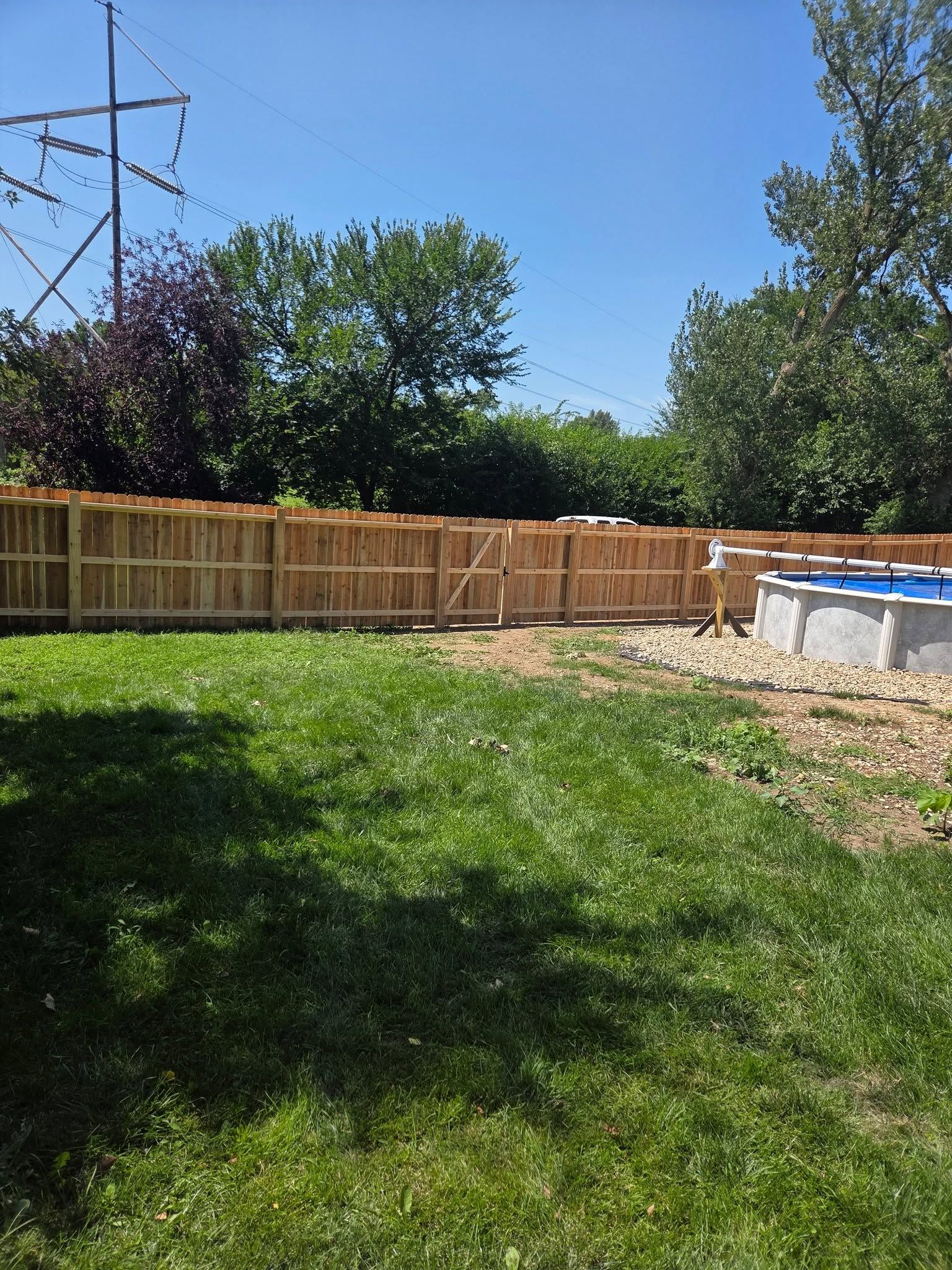 Sunny backyard with green lawn, wooden fence, trees, and a small above-ground pool