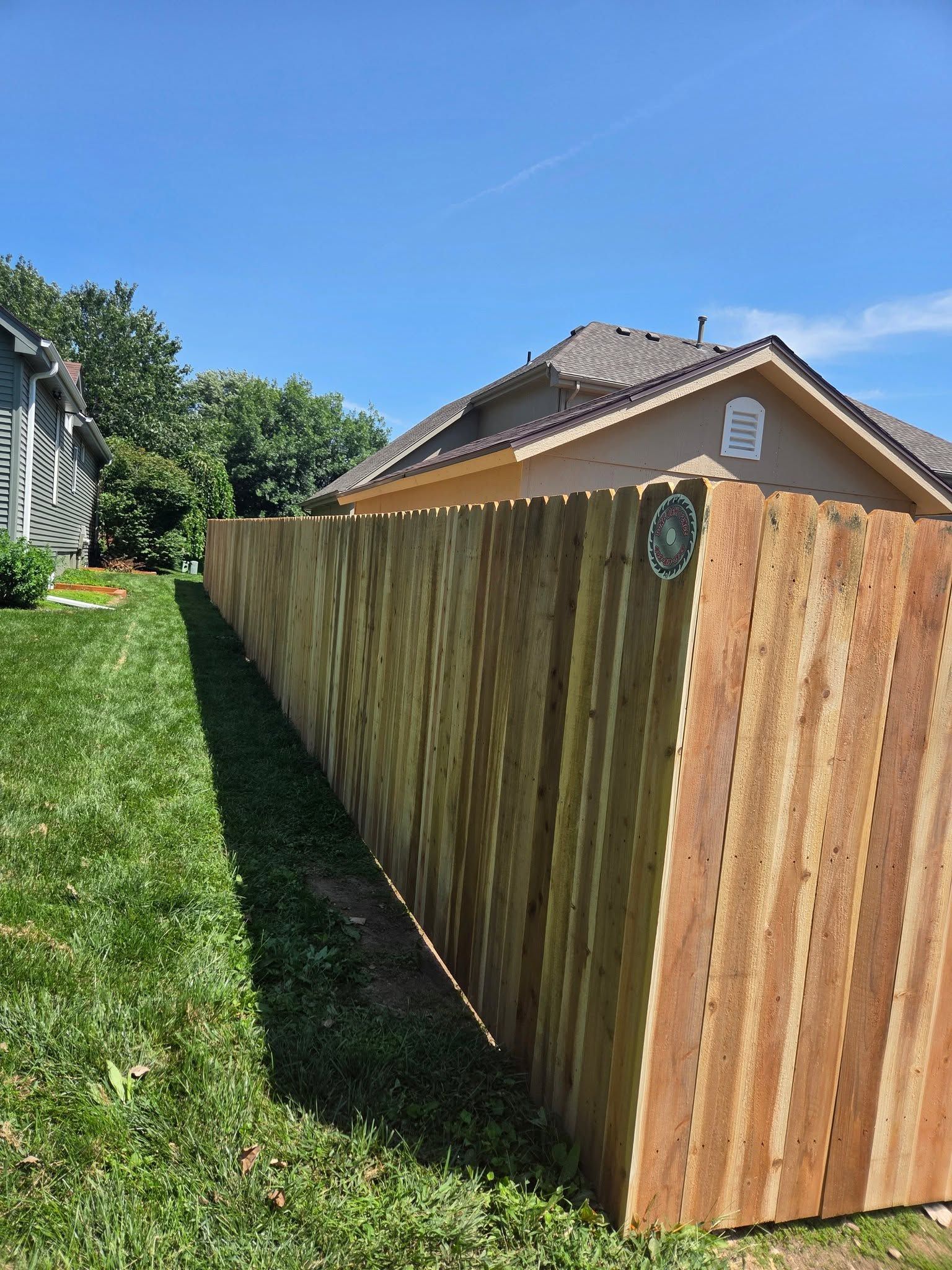 Wooden privacy fence along a grassy yard beside a house under a clear blue sky