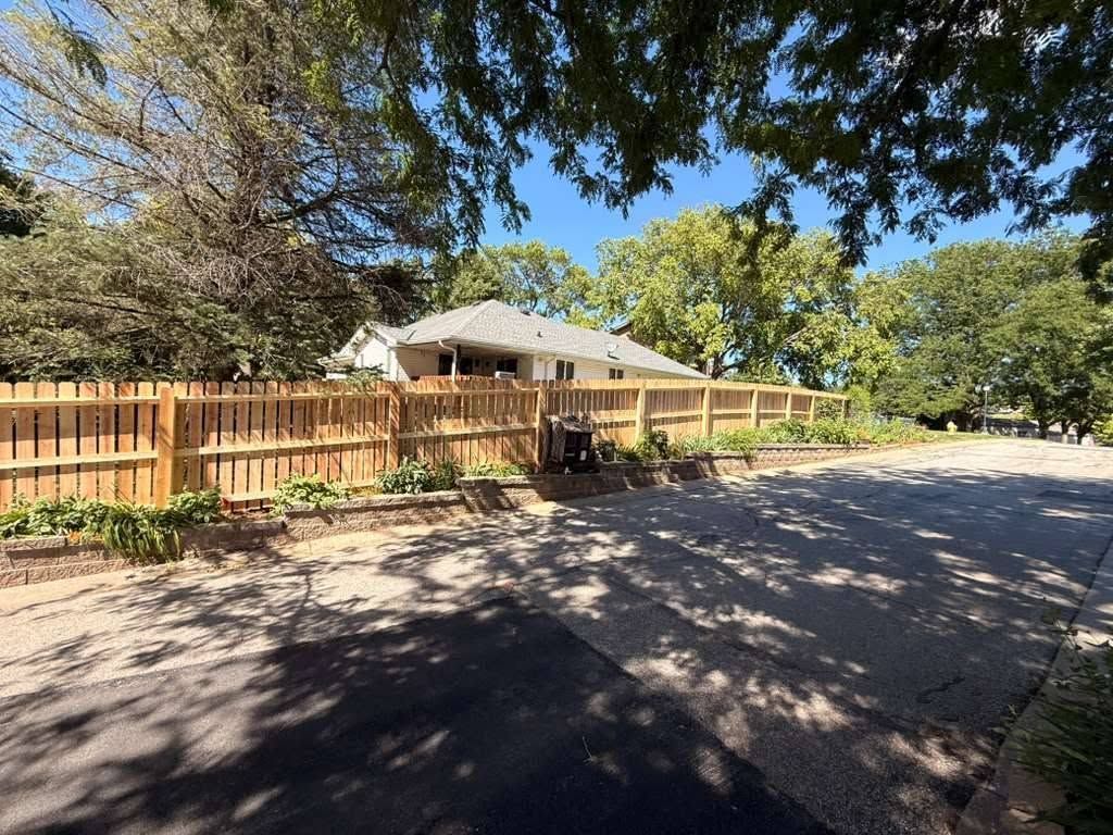 Wooden fence beside a house with a shaded driveway and trees overhead