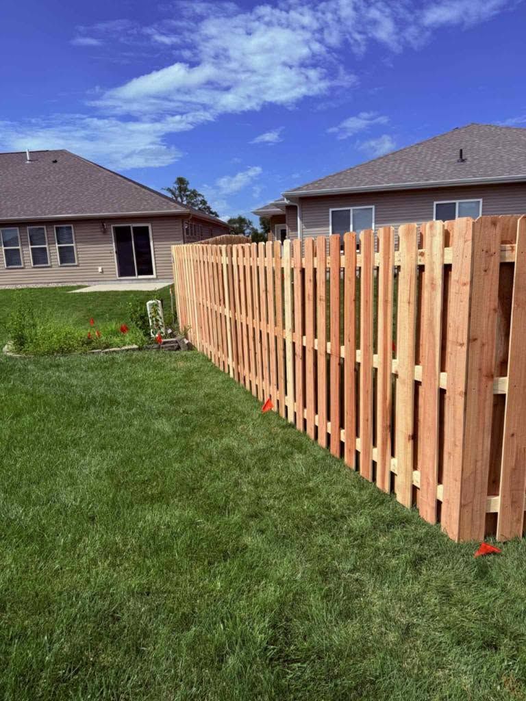 Wooden privacy fence along a green lawn beside suburban houses under a blue sky
