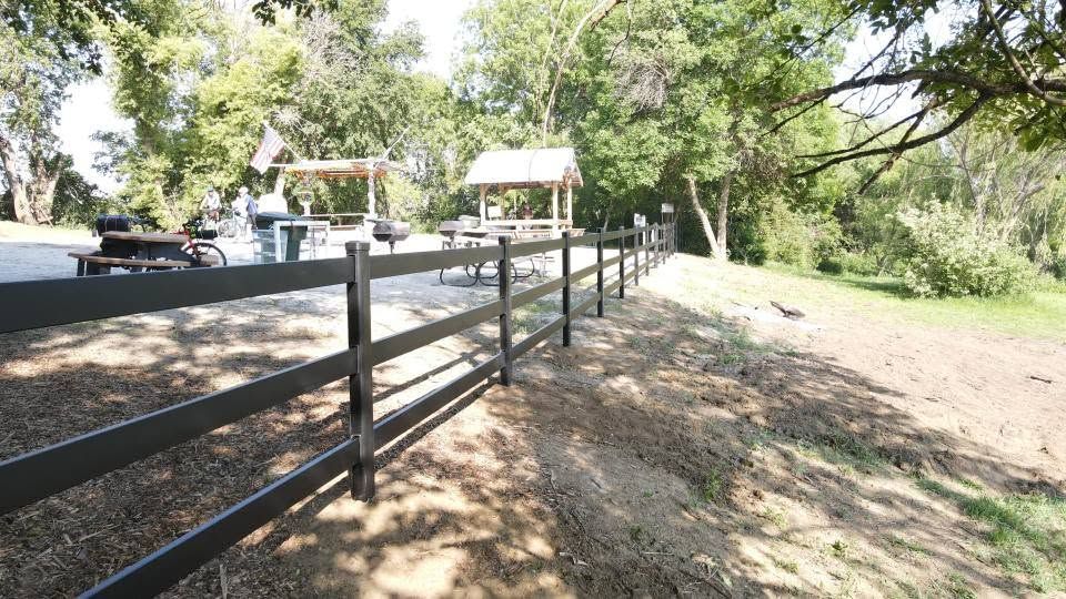 Wooden fence along a shaded dirt path beside a quiet road and trees