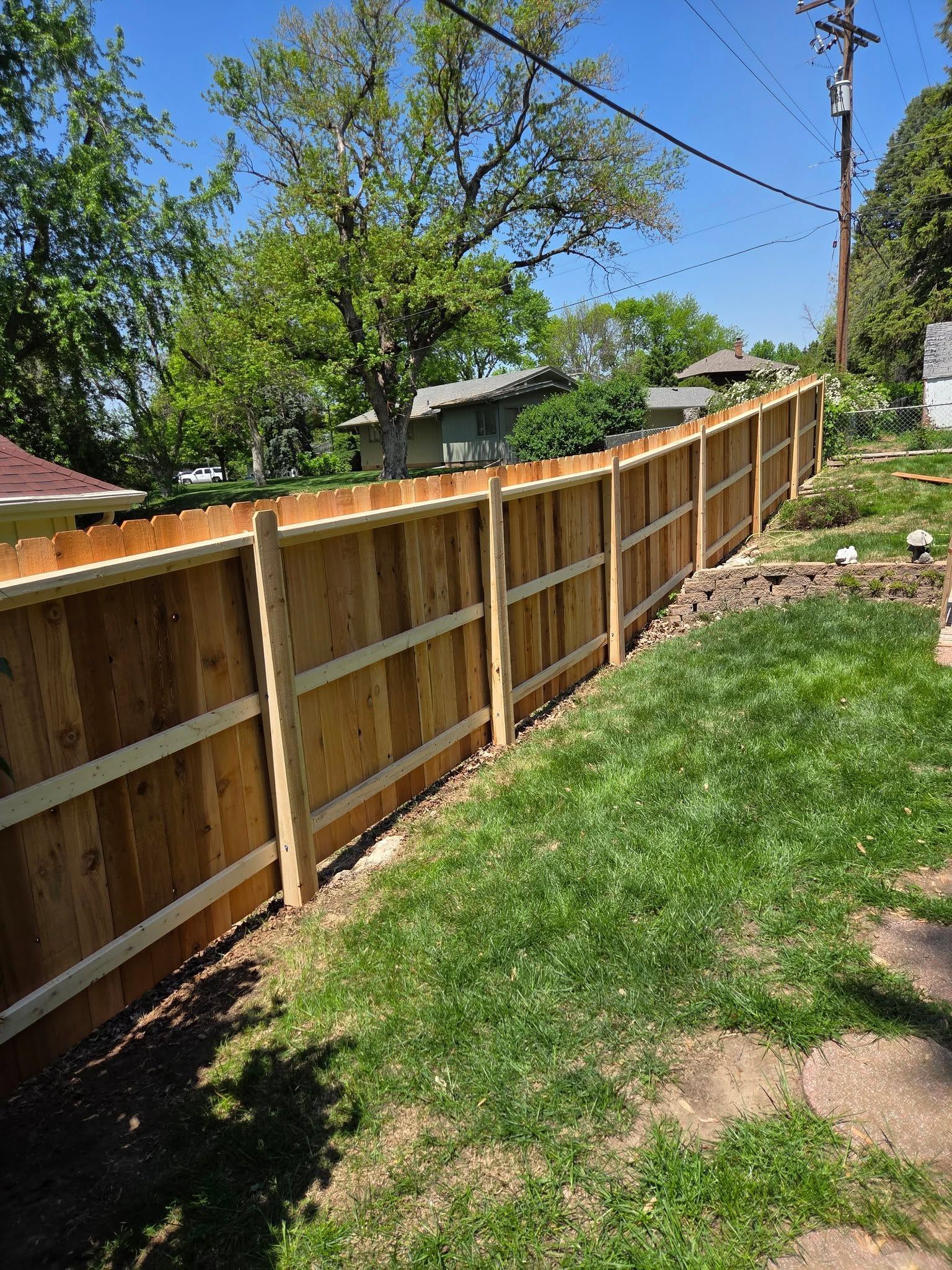 Wooden fence along a grassy backyard path under a bright blue sky