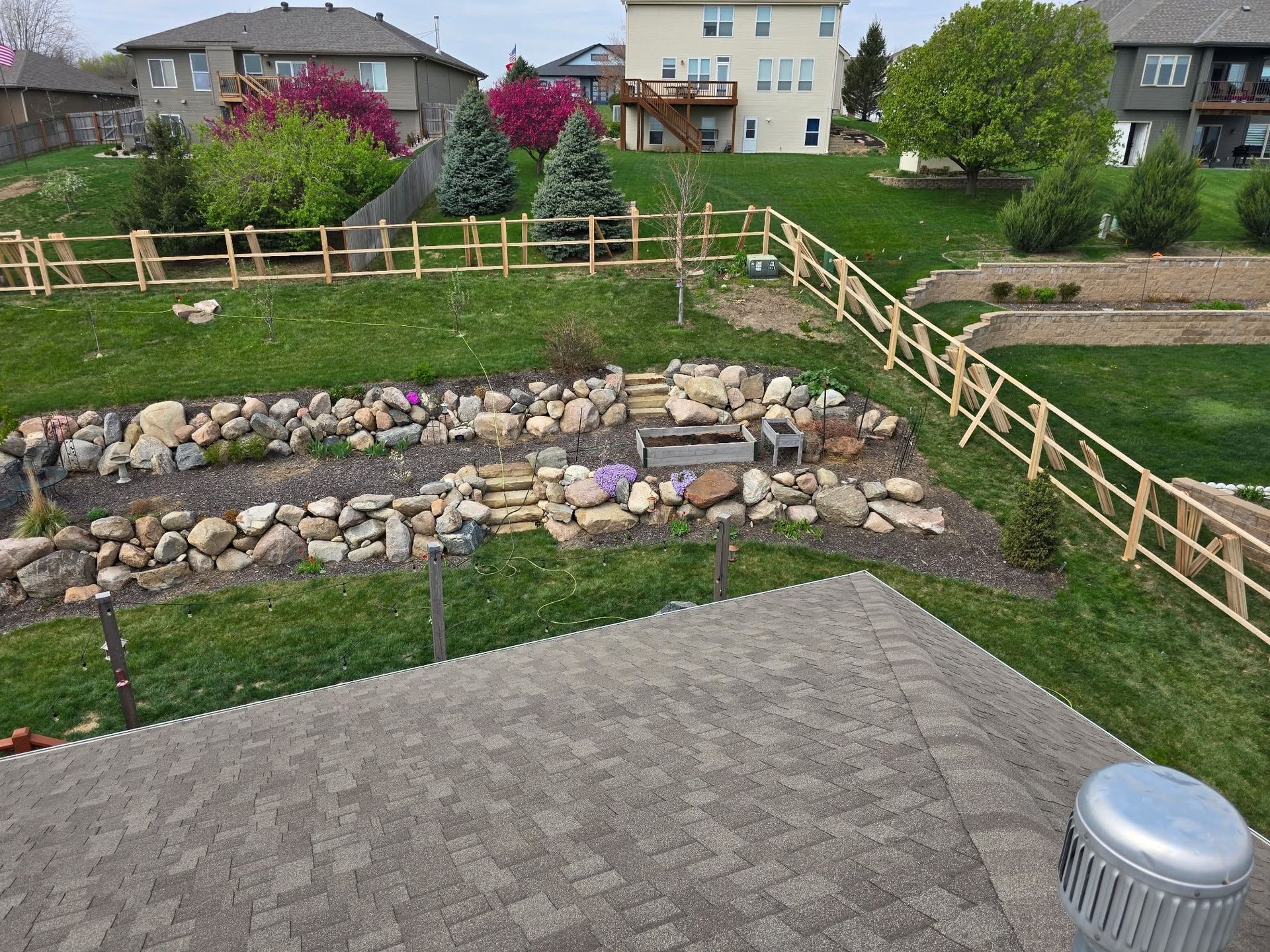 Terraced rock garden with wooden fences, green grass, and houses in the background.