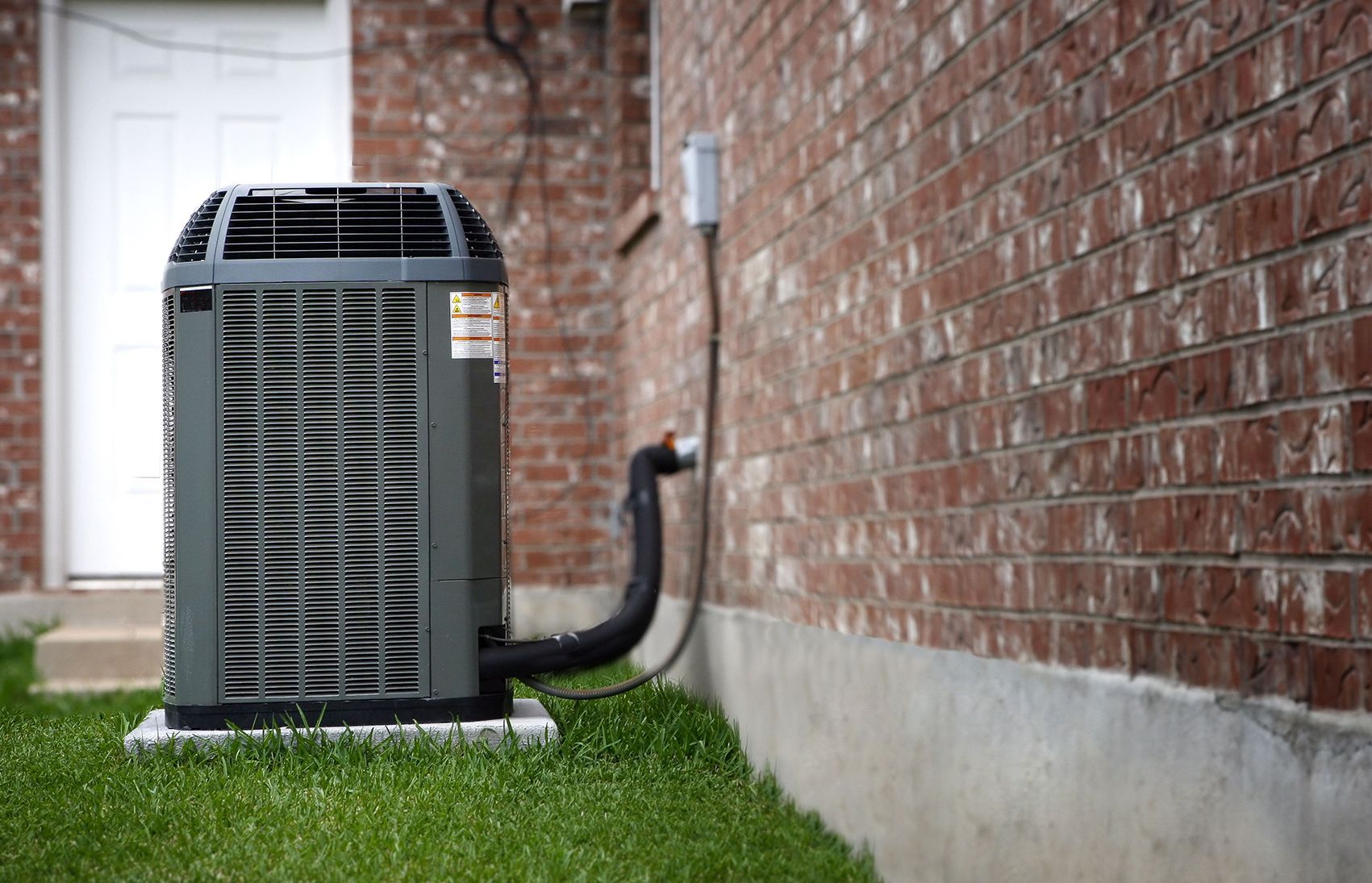 Outdoor air conditioner unit beside a brick house wall on a grassy lawn