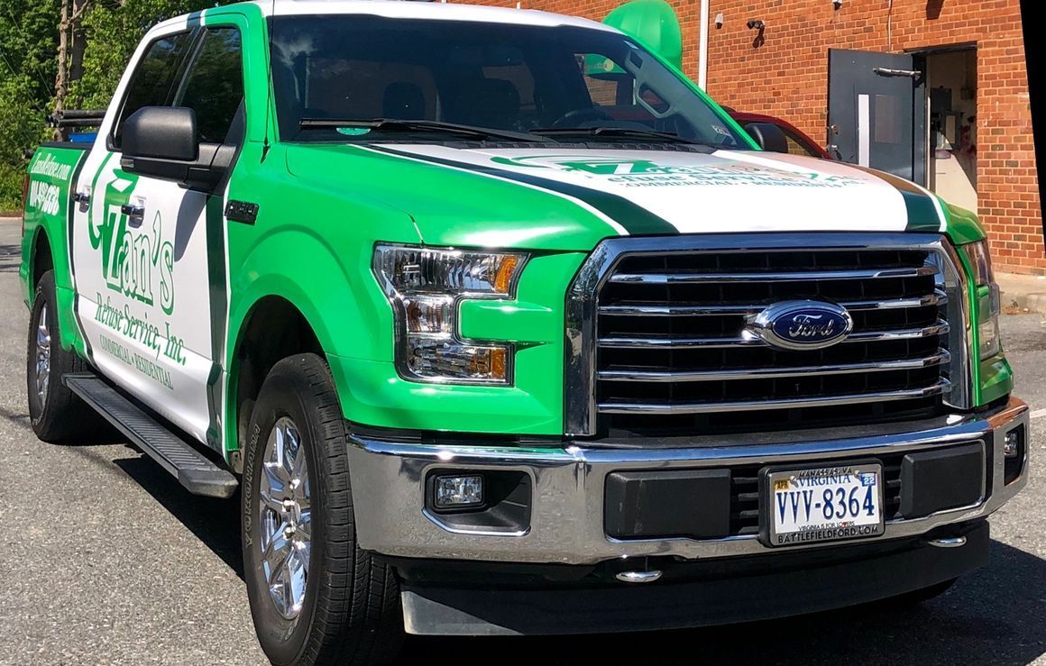 A bright green and white Ford pickup truck branded with logo and text, parked in front of a brick building.