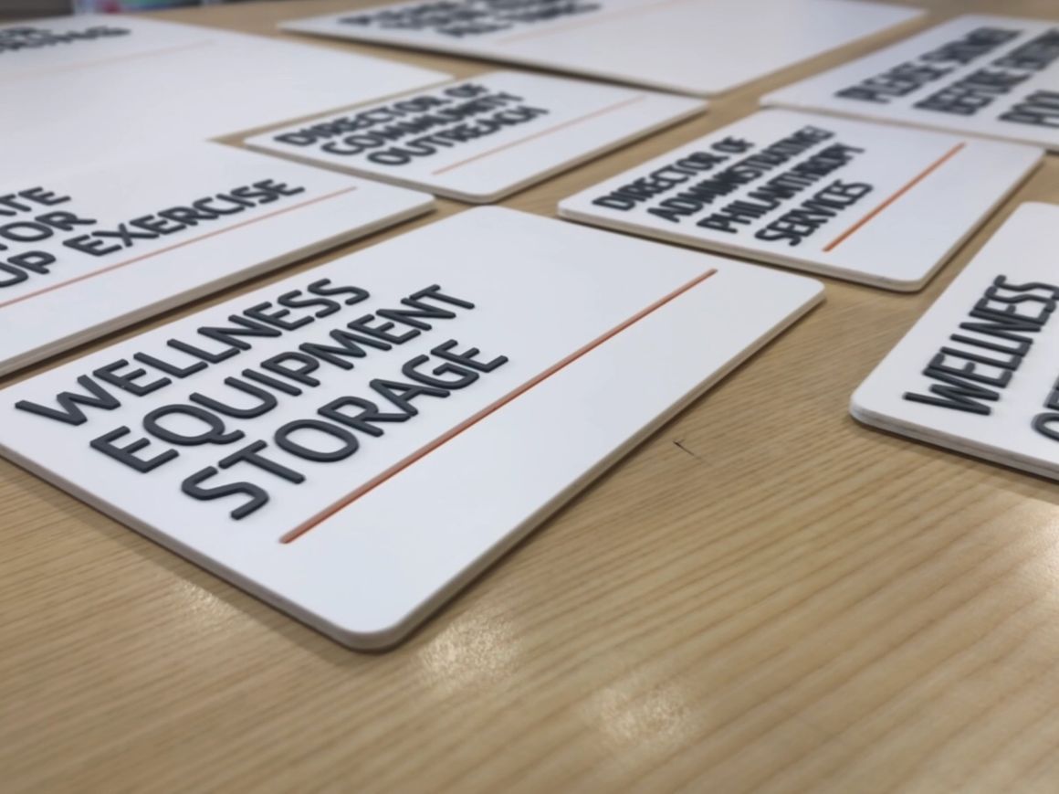 Several white signage plaques with black text and orange lines laid out on a light wood surface.