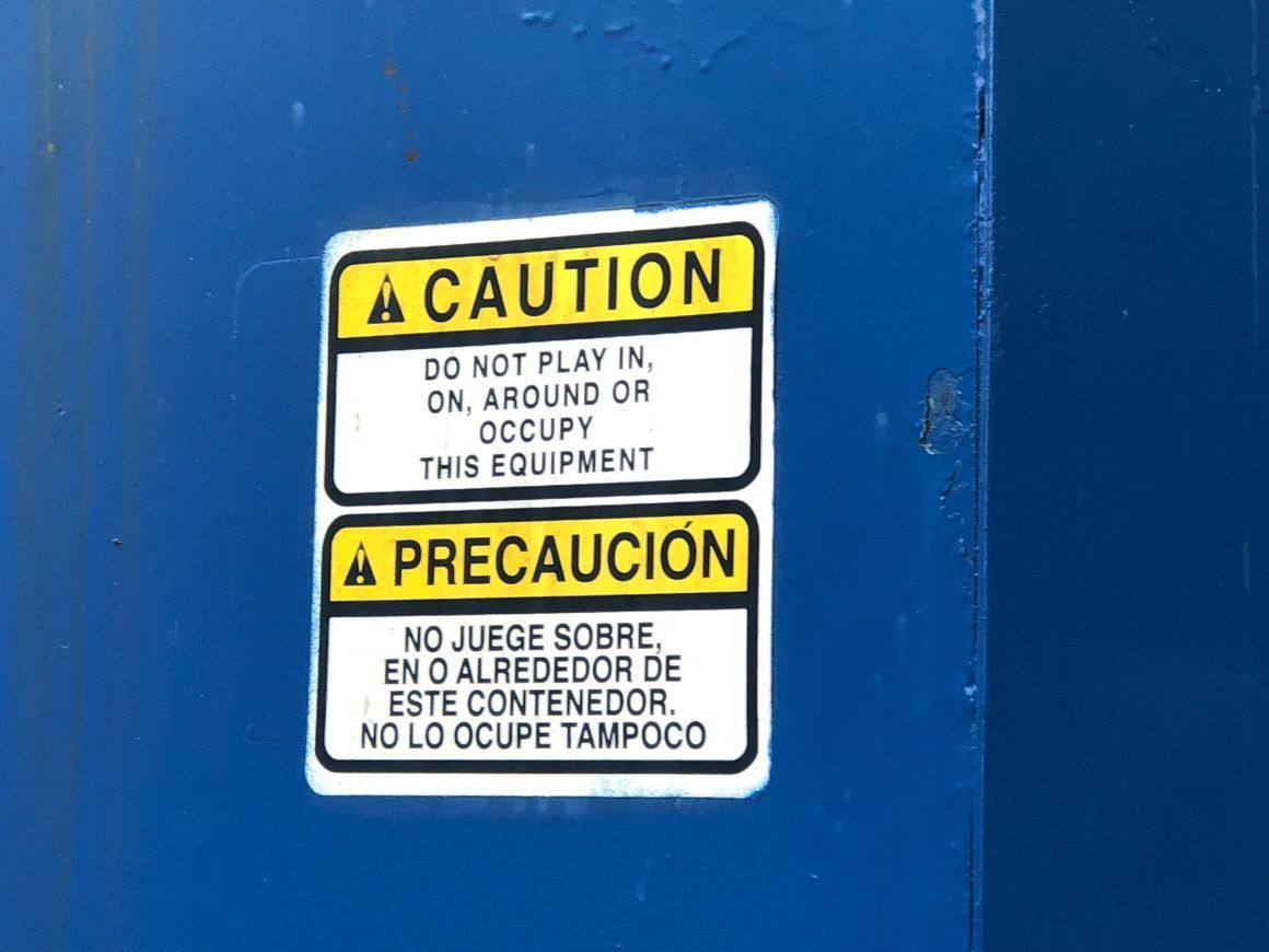 A caution sign in English and Spanish on a blue surface warning people not to play in, on, or around the equipment.
